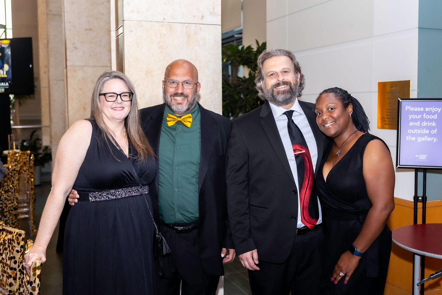 Four formally dressed guests pose together at an evening social function with decorative elements visible.