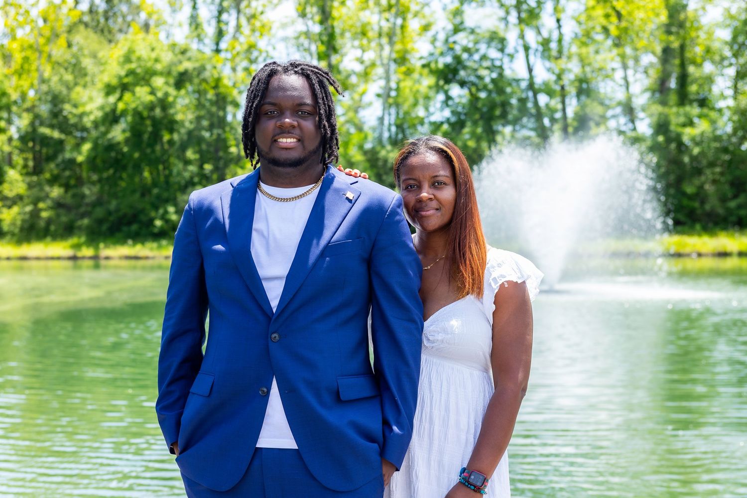 Happy couple smiles while posing together near a lake with fountain spray.