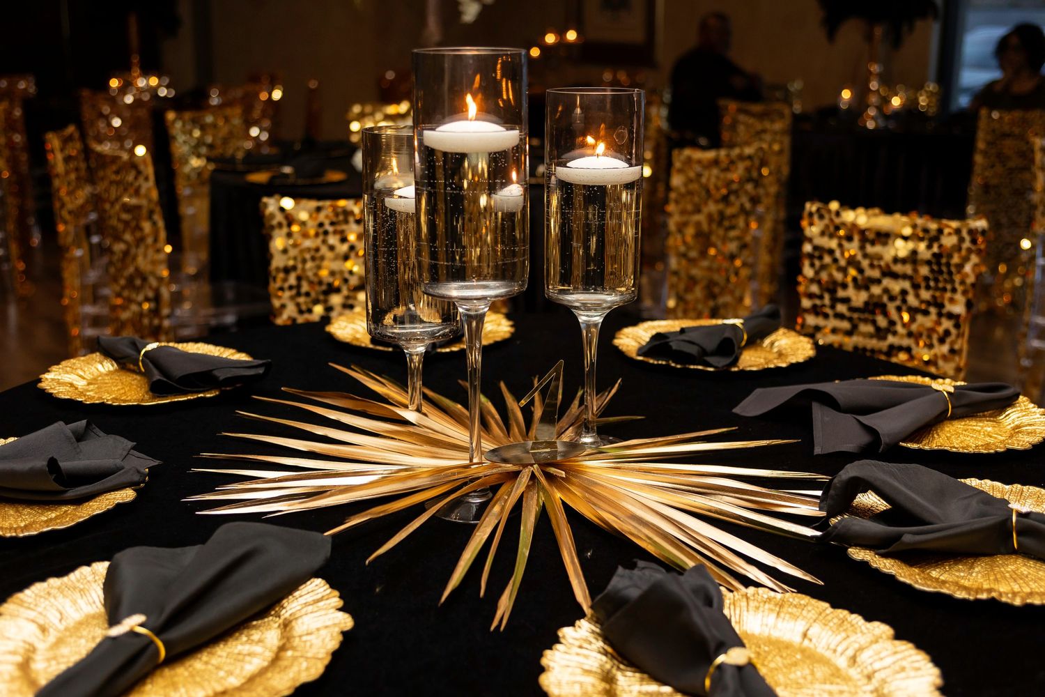 Elegant table setting with black and gold decor featuring floating candles and metallic accents.