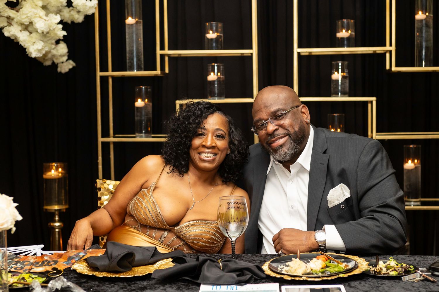 A couple enjoying dinner at an elegant event with gold geometric decorations and white flowers.