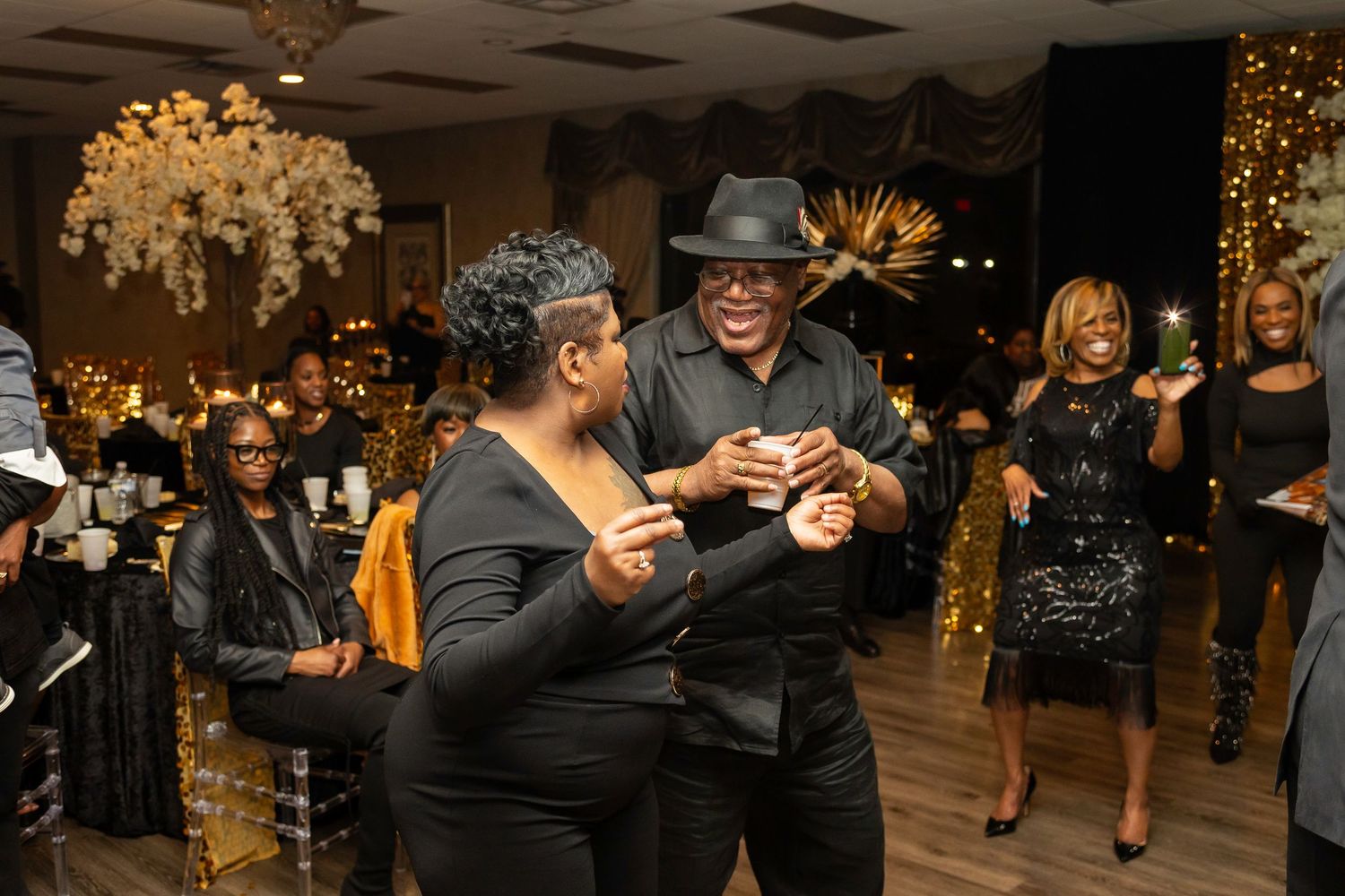 Party guests dancing and socializing at an elegant indoor event with chandelier lighting.