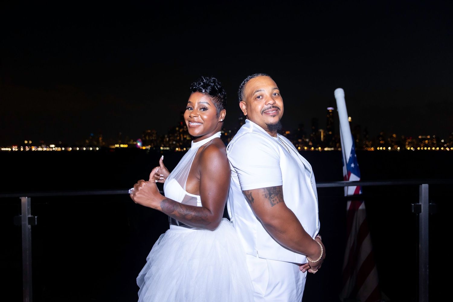 Nighttime celebration with party guests in white attire posing against city lights.