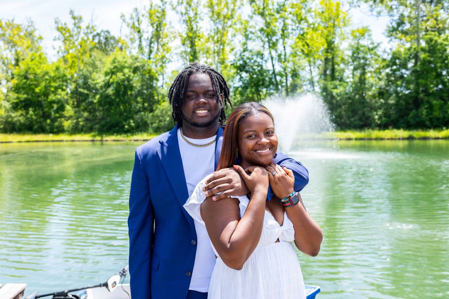 Joyful couple embraces while laughing by scenic lake with fountain.