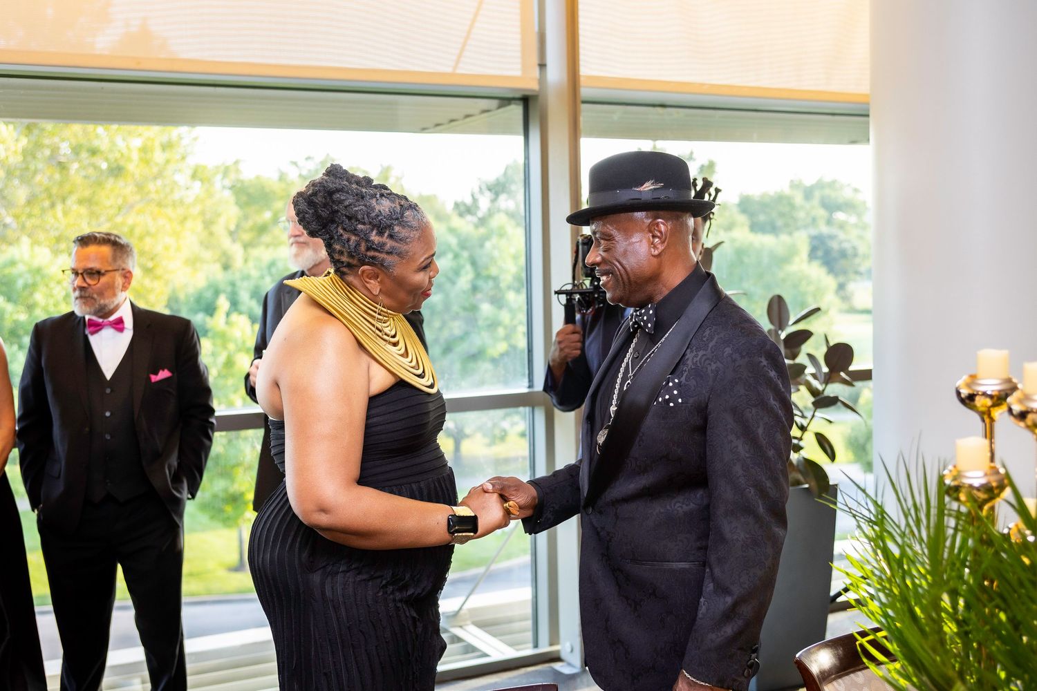 Guests interact during formal evening event with window views in background.