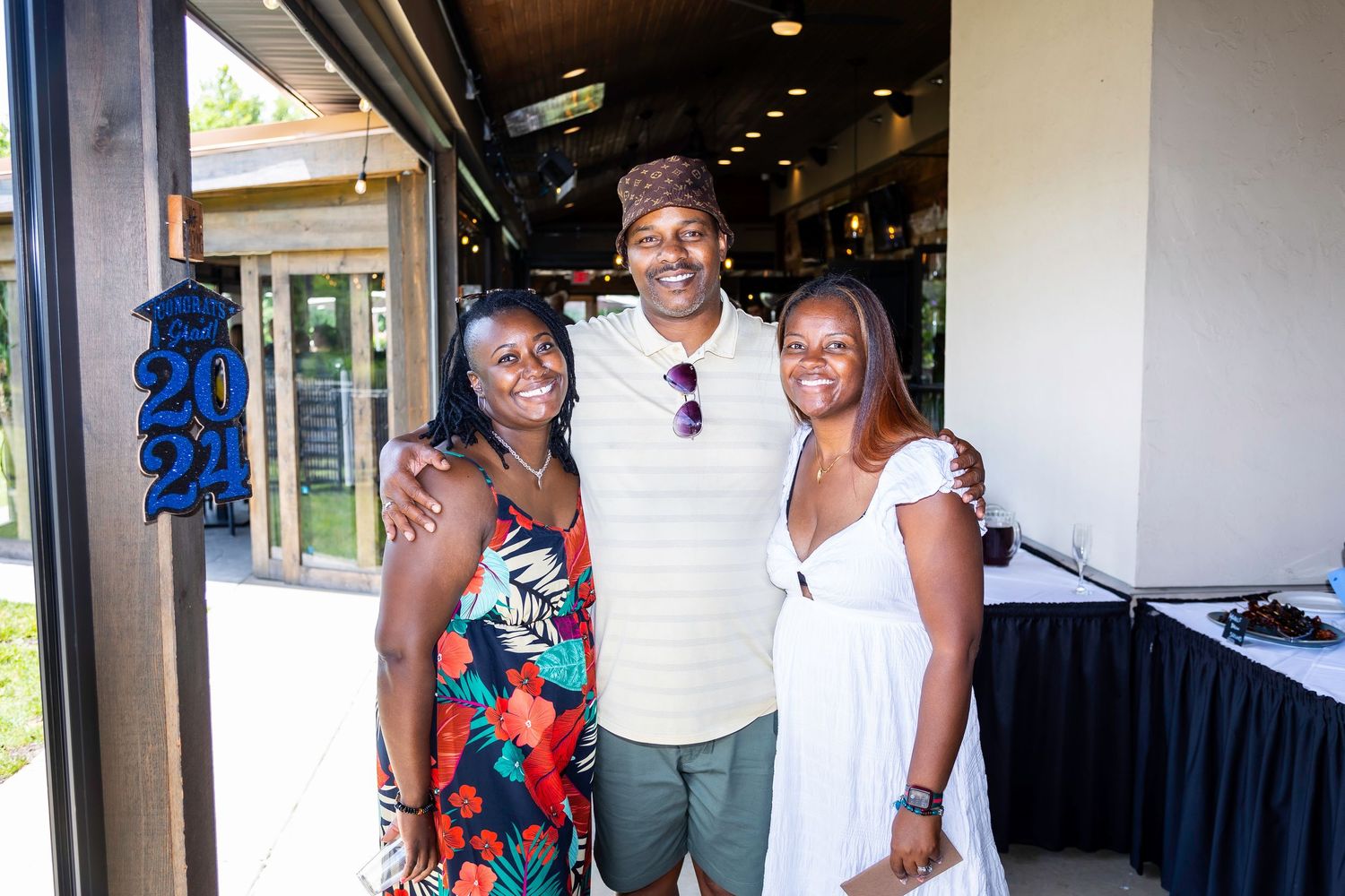 Three people pose together at an event wearing casual summer attire.