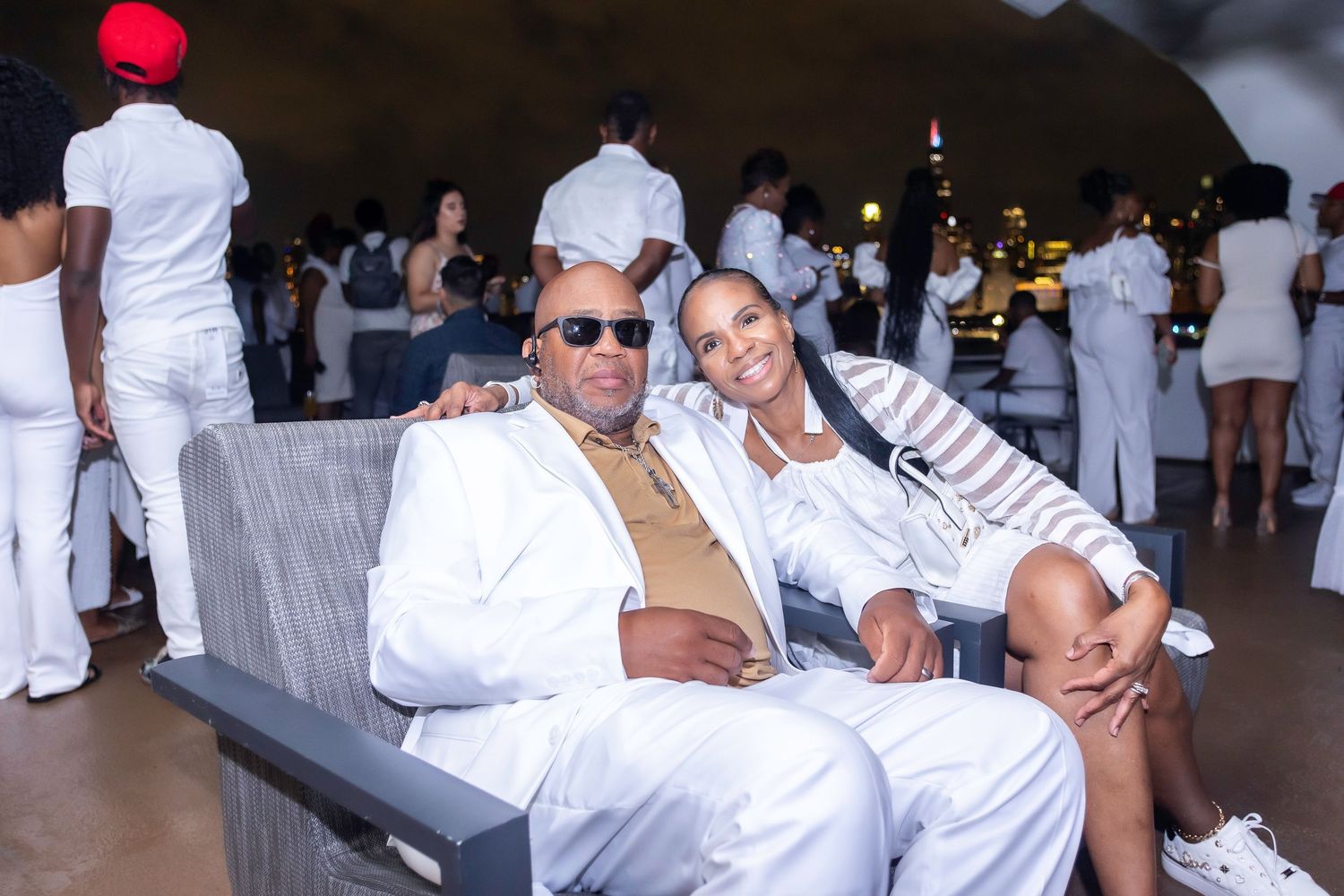 Party guests dressed in white relaxing on gray couch at an indoor event.
