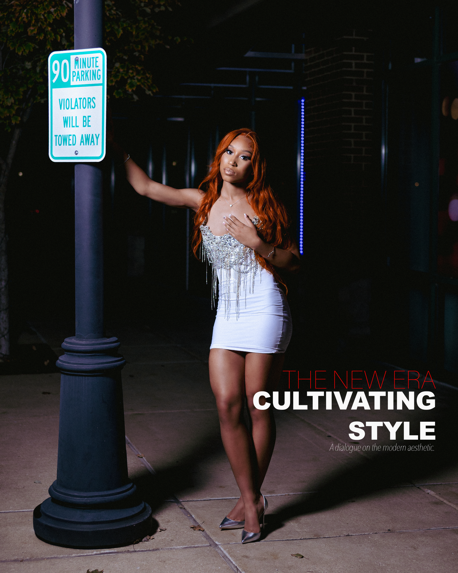 Woman in white mini dress with red hair poses by a street pole at night for The New Era Cultivating Style magazine.