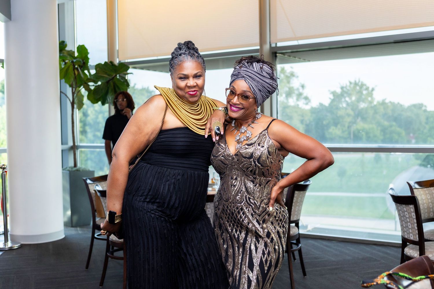 Two guests in formal black and metallic dresses pose at evening celebration.