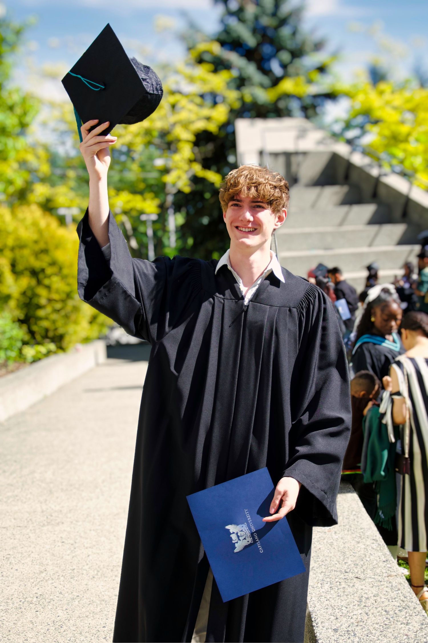 Male in graduation gown holding certificate and cap, Graduation, north Vancouver, University