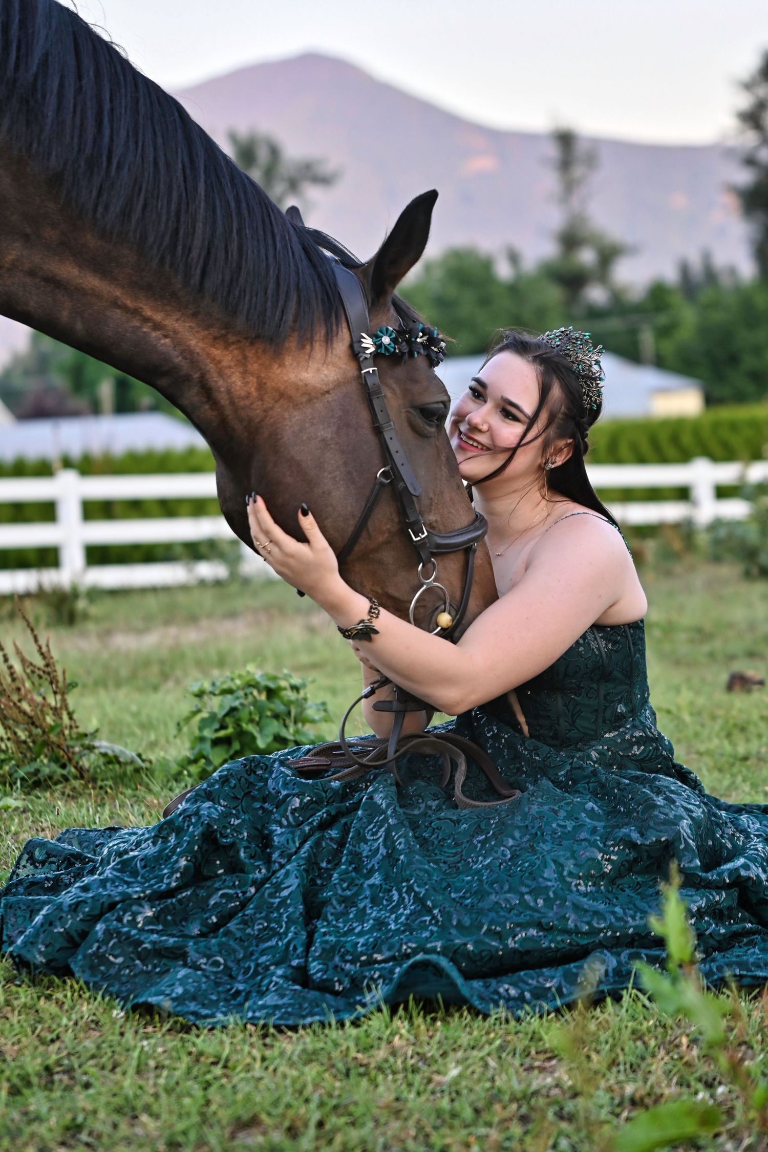 Female in green grad gown sitting on the ground hugging a horse's head, equine, graduation, Fraser Valley
