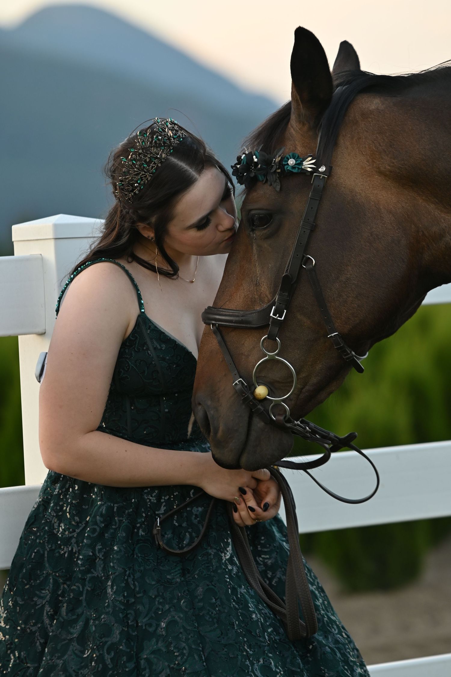 Female in green grad dress kissing bay horse's head
