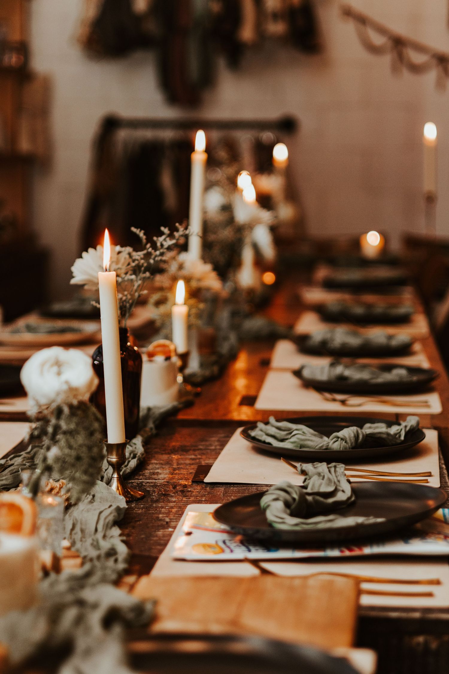 Candlelit wedding reception table with taper candles, dark plates, sage green napkins and rustic floral decor.