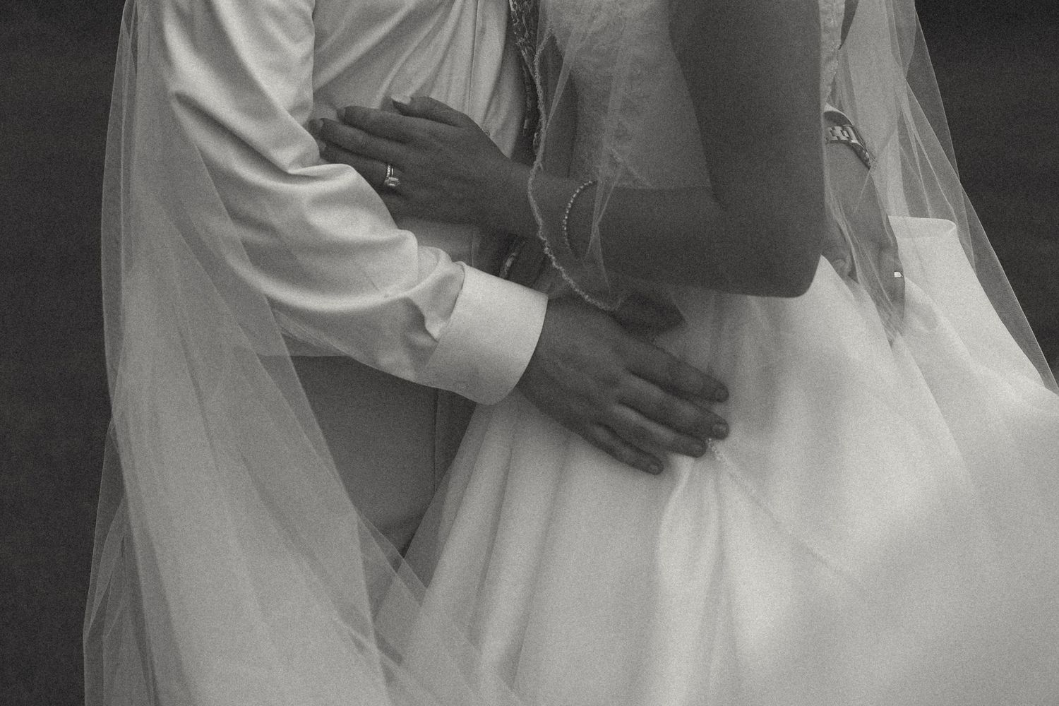 Black and white close-up of a bride and groom embracing, with the sheer veil and flowing wedding gown draped around them.