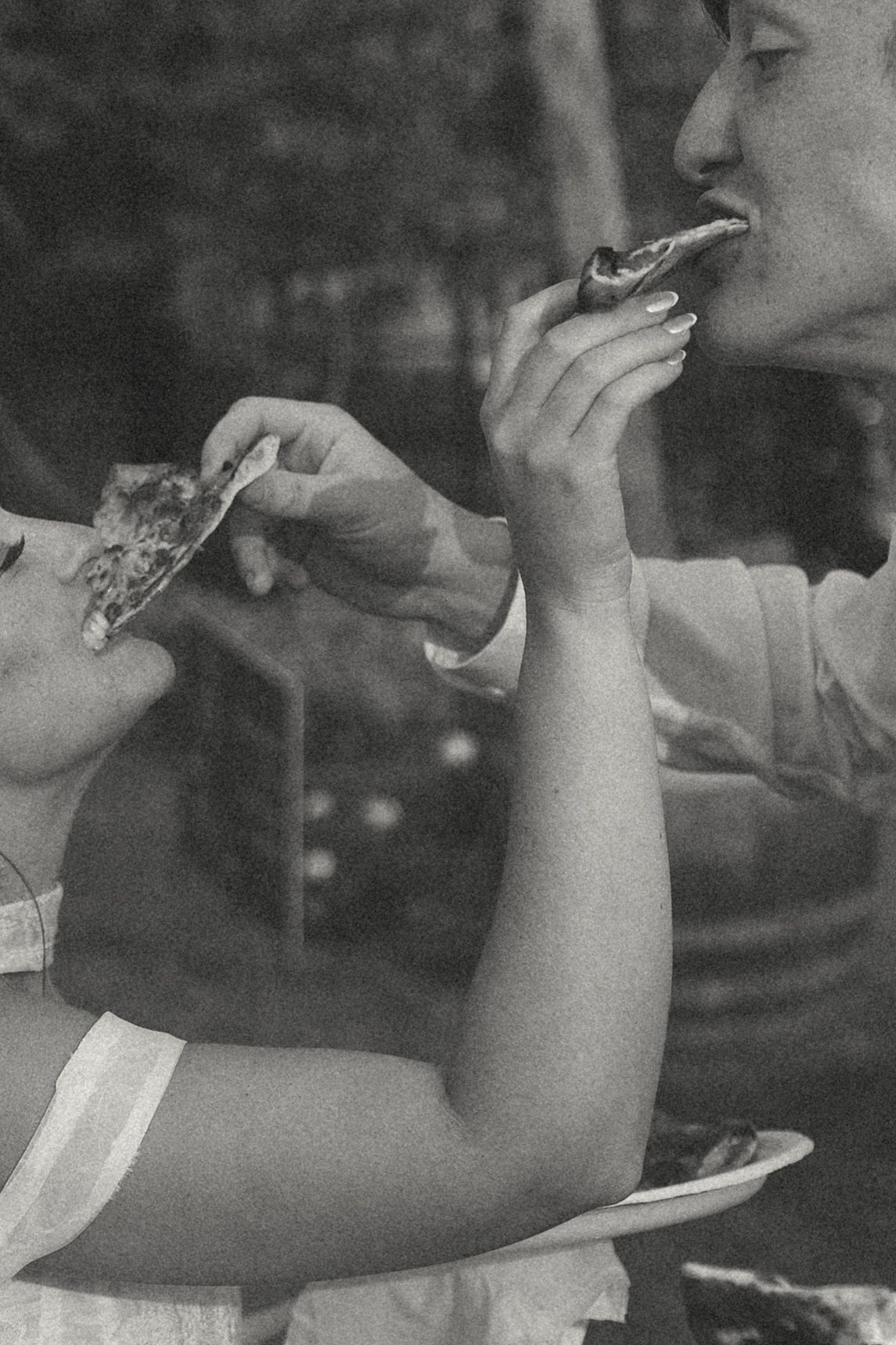 Black and white close-up of a bride and groom feeding each other slices of pizza at their wedding celebration.