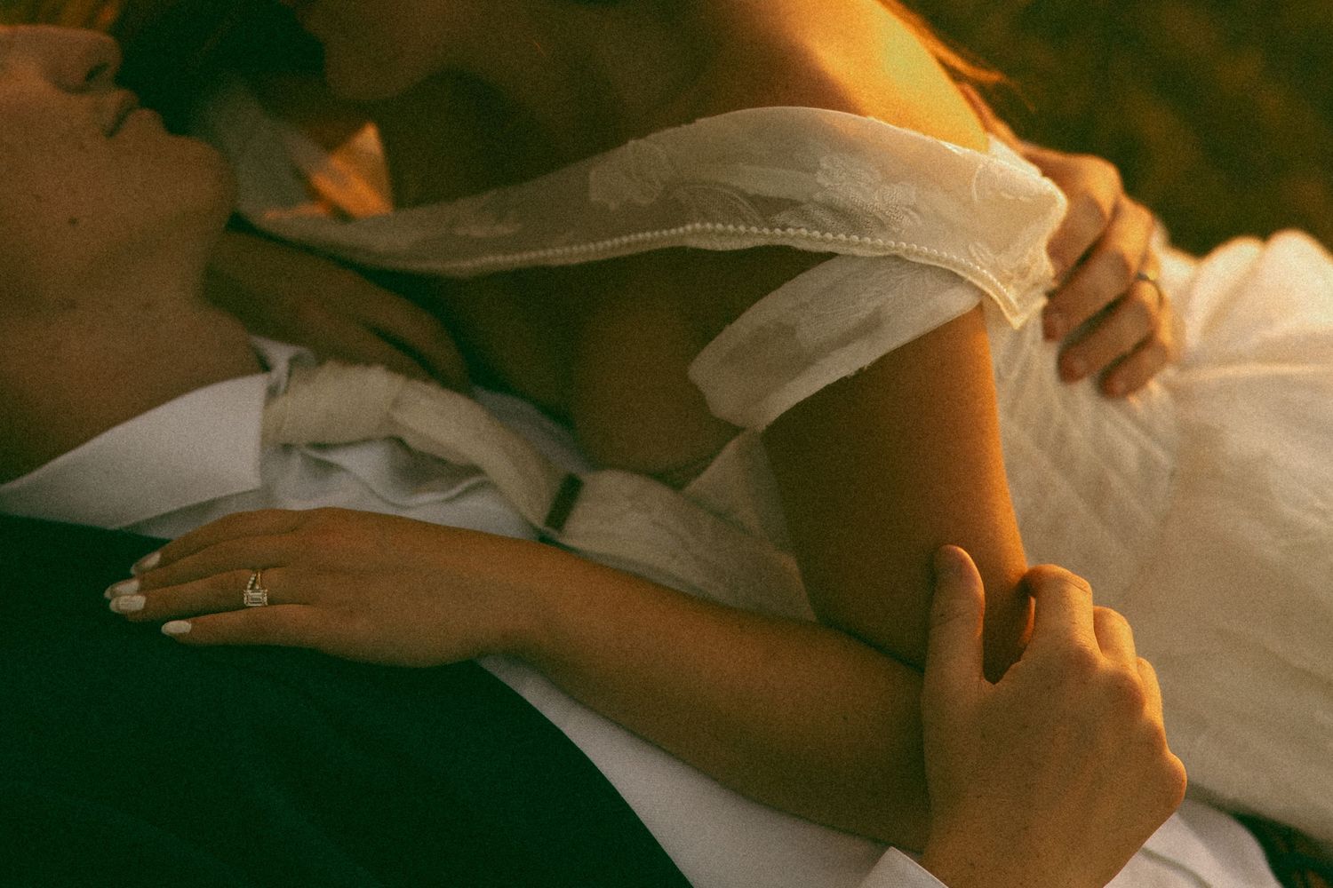 Intimate close-up of a bride embracing her groom, showing her wedding ring and the soft off-shoulder neckline of her dress.