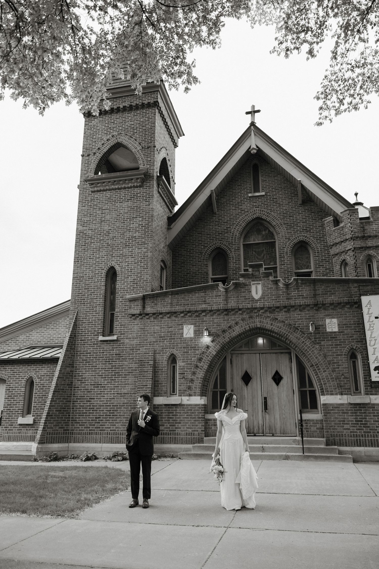 Black and white photo of a bride and groom standing outside a historic brick church on their wedding day.