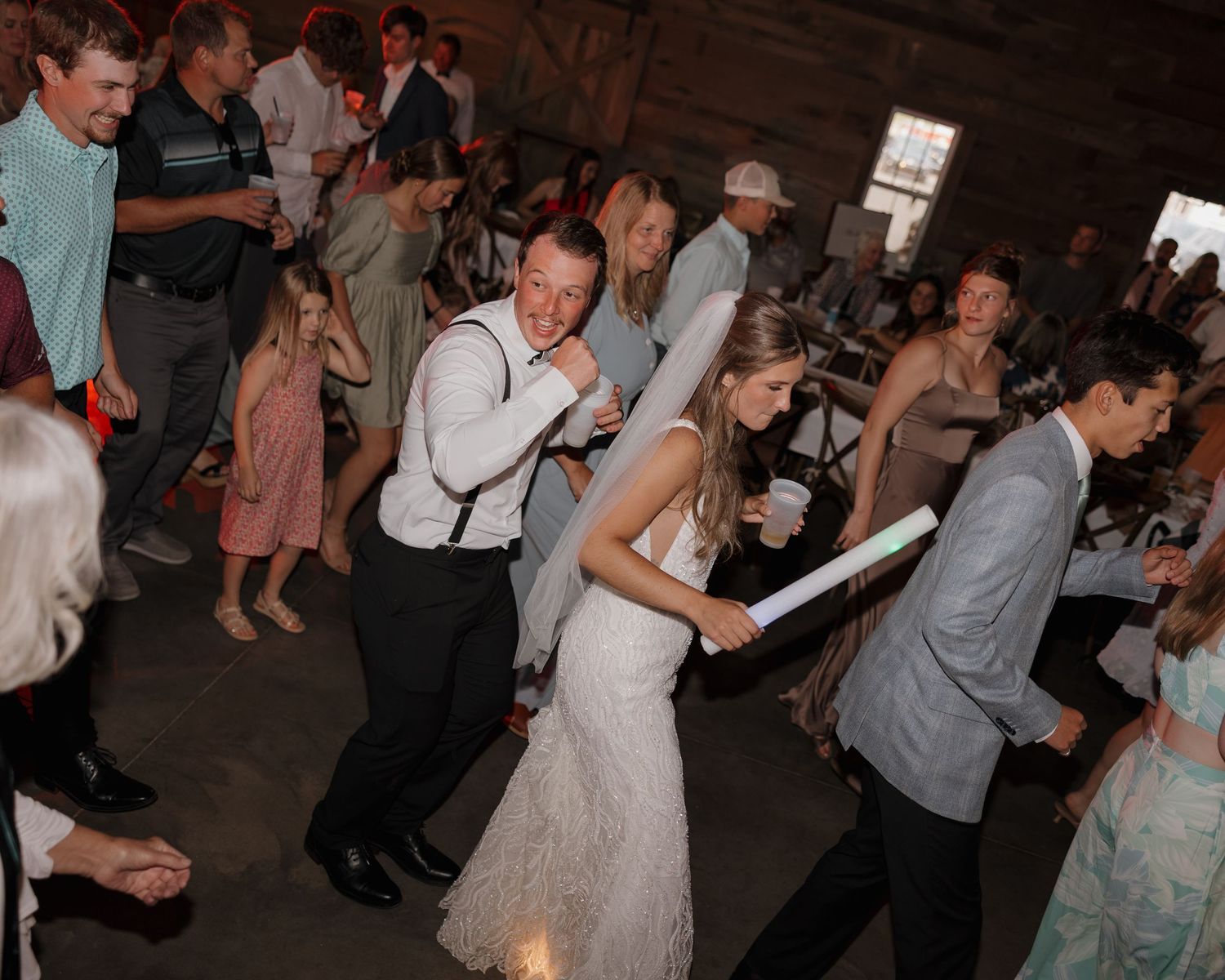 Wedding guests dance together during a lively reception celebration in a dimly lit venue.