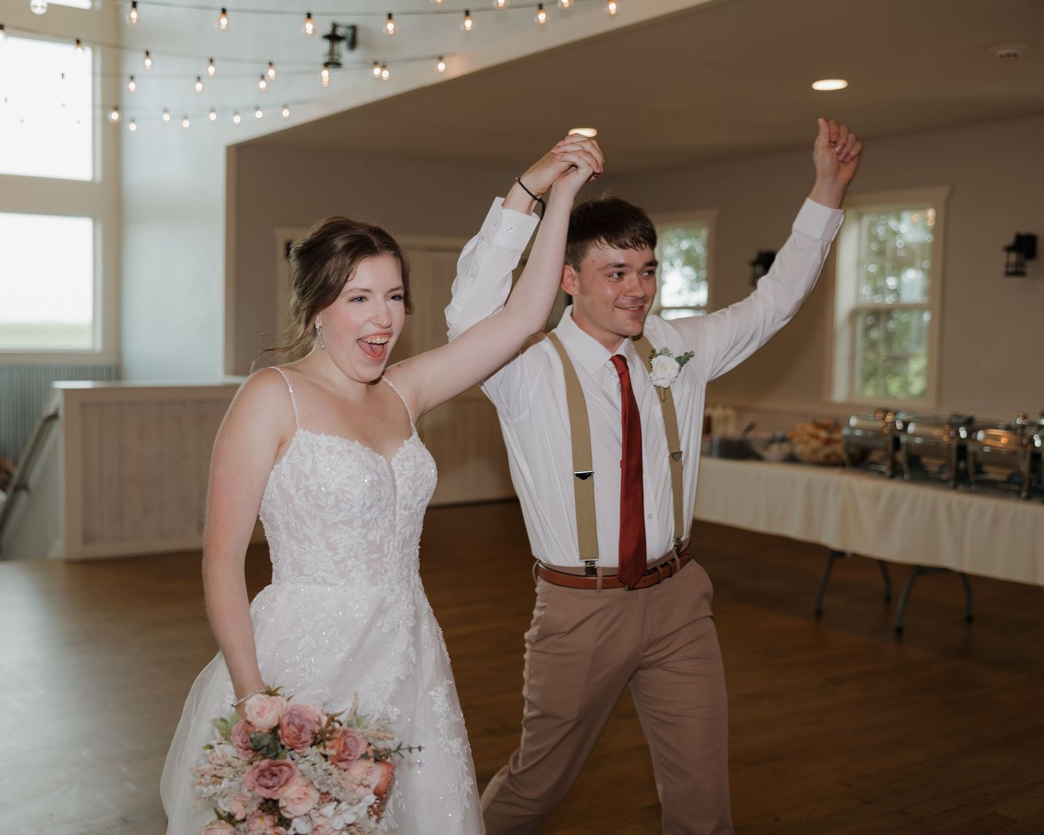 A couple celebrates joyfully during their first dance at a rustic barn wedding reception with string lights overhead.