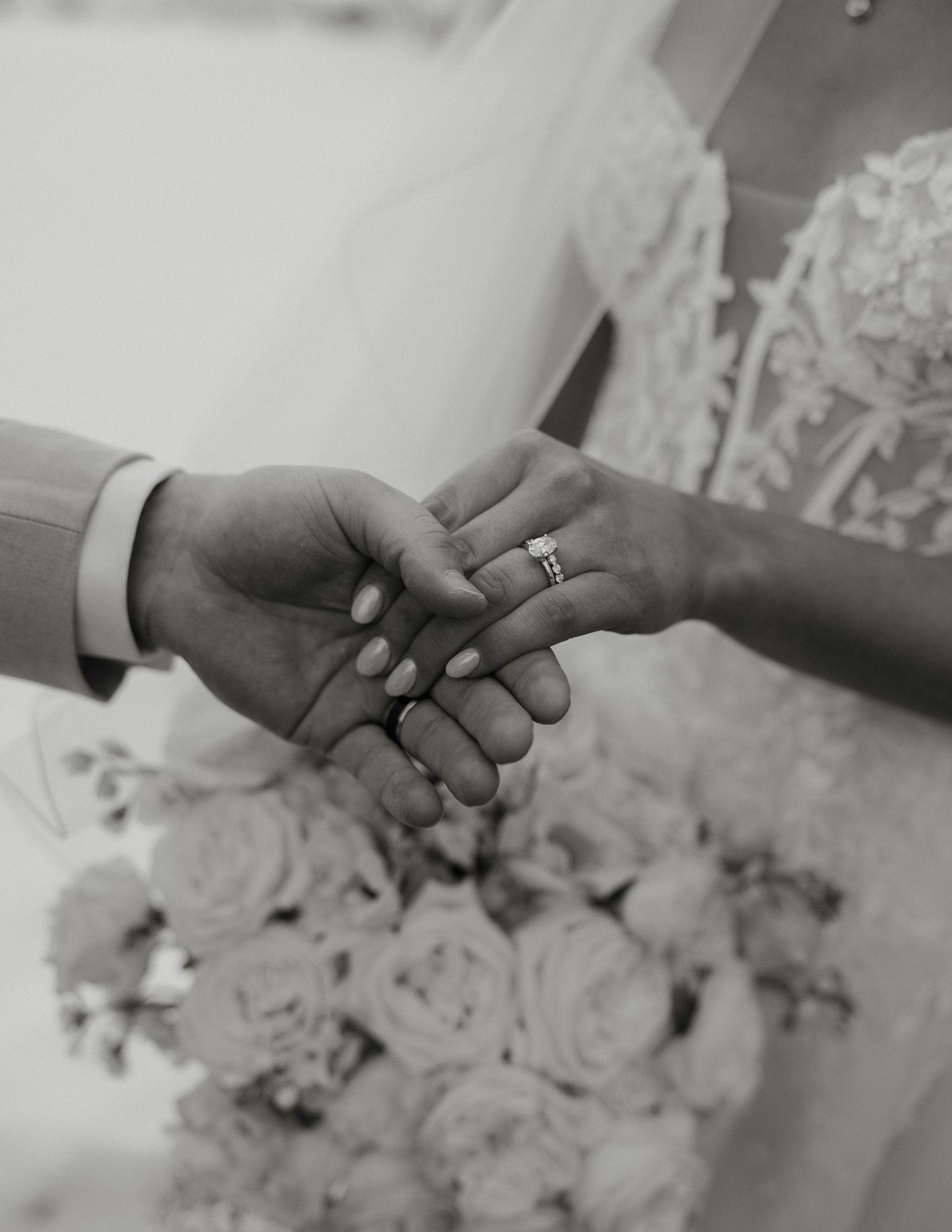 Close-up black and white shot of hands exchanging wedding rings during a romantic ceremony.