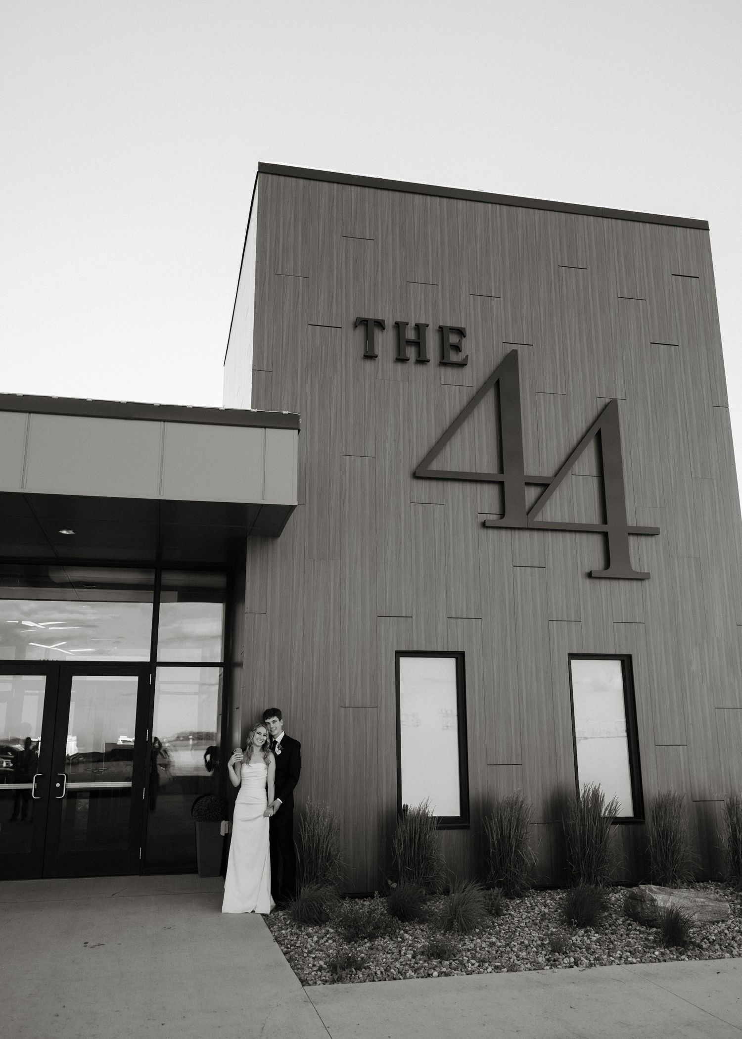 Black and white photo of a bride and groom posing outside The 44 wedding venue at dusk.