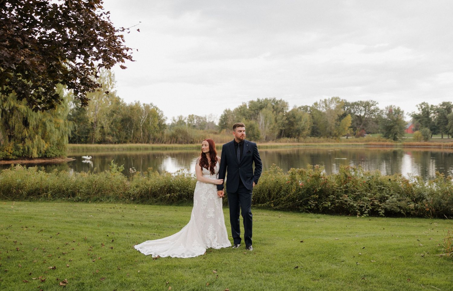 A scenic outdoor wedding ceremony in a lush green field surrounded by autumn trees and natural landscape.