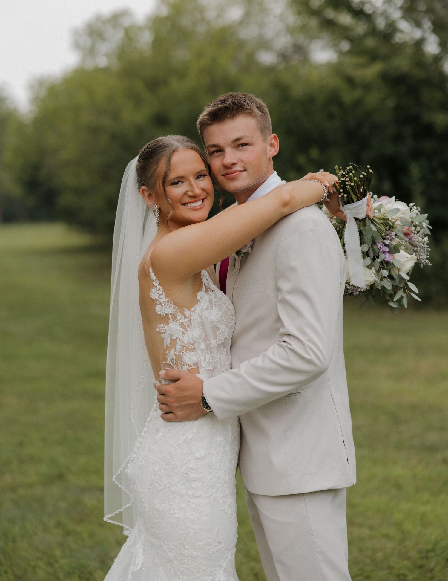 A couple shares joyful moments in their wedding attire while posing outdoors in a natural setting.