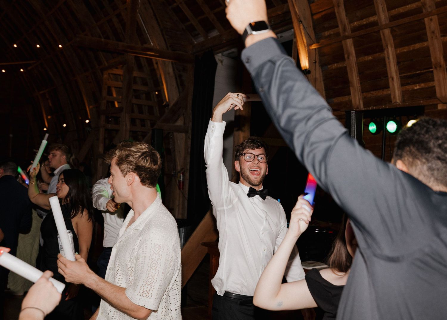 Dancers move energetically on a dark dance floor at a party celebration with arms raised in joyful motion.
