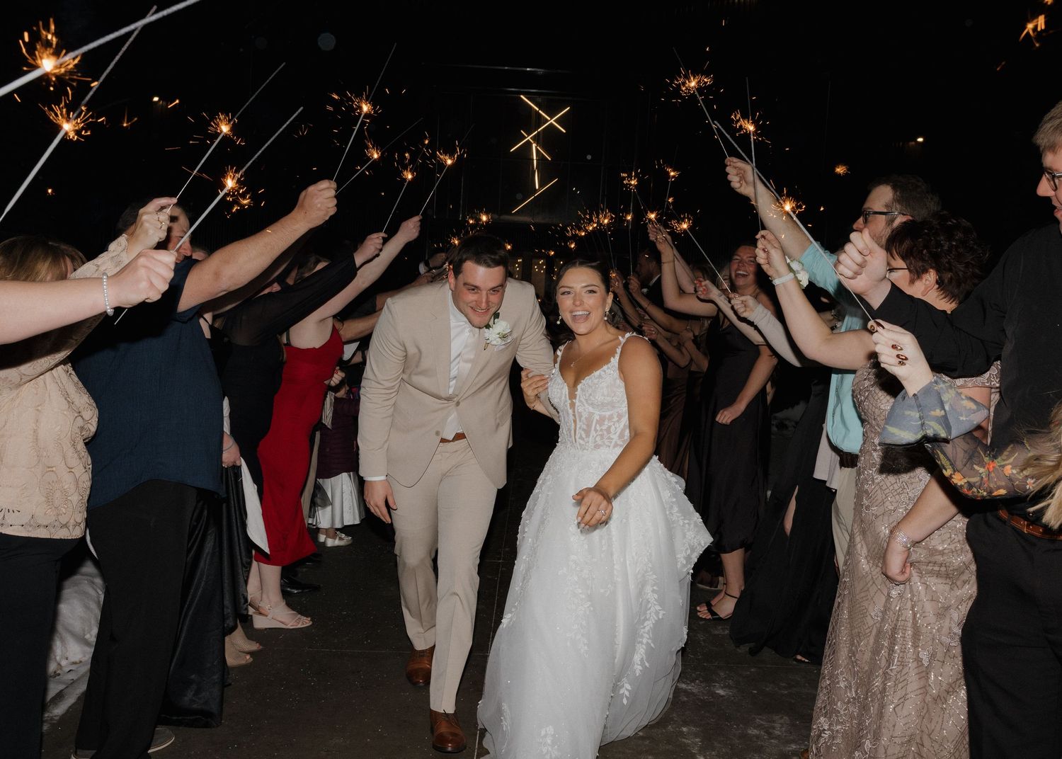 Wedding guests dance and celebrate with sparklers on a dark dance floor during an evening reception.