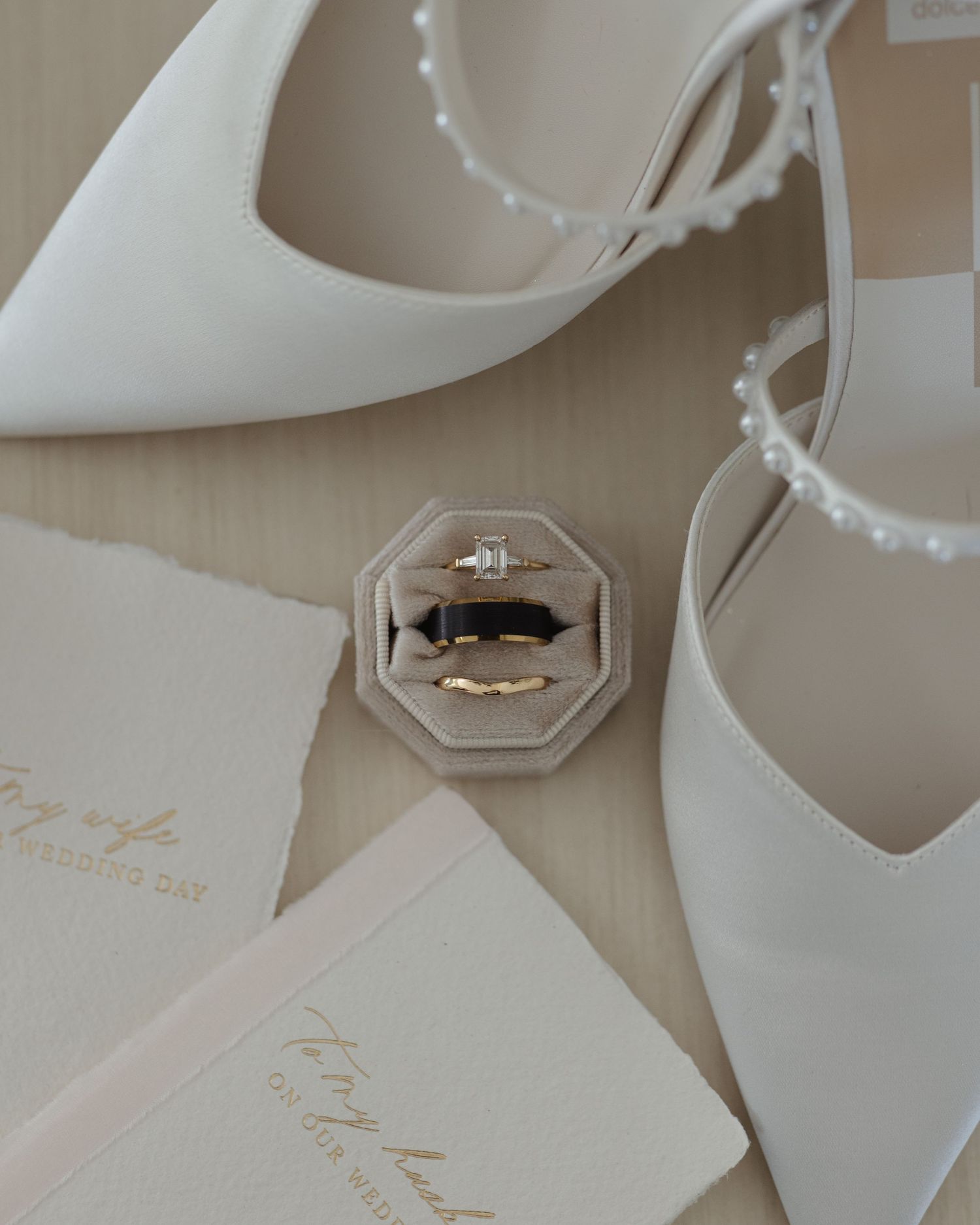 Wedding accessories including elegant white invitations and jewelry box on beige surface.