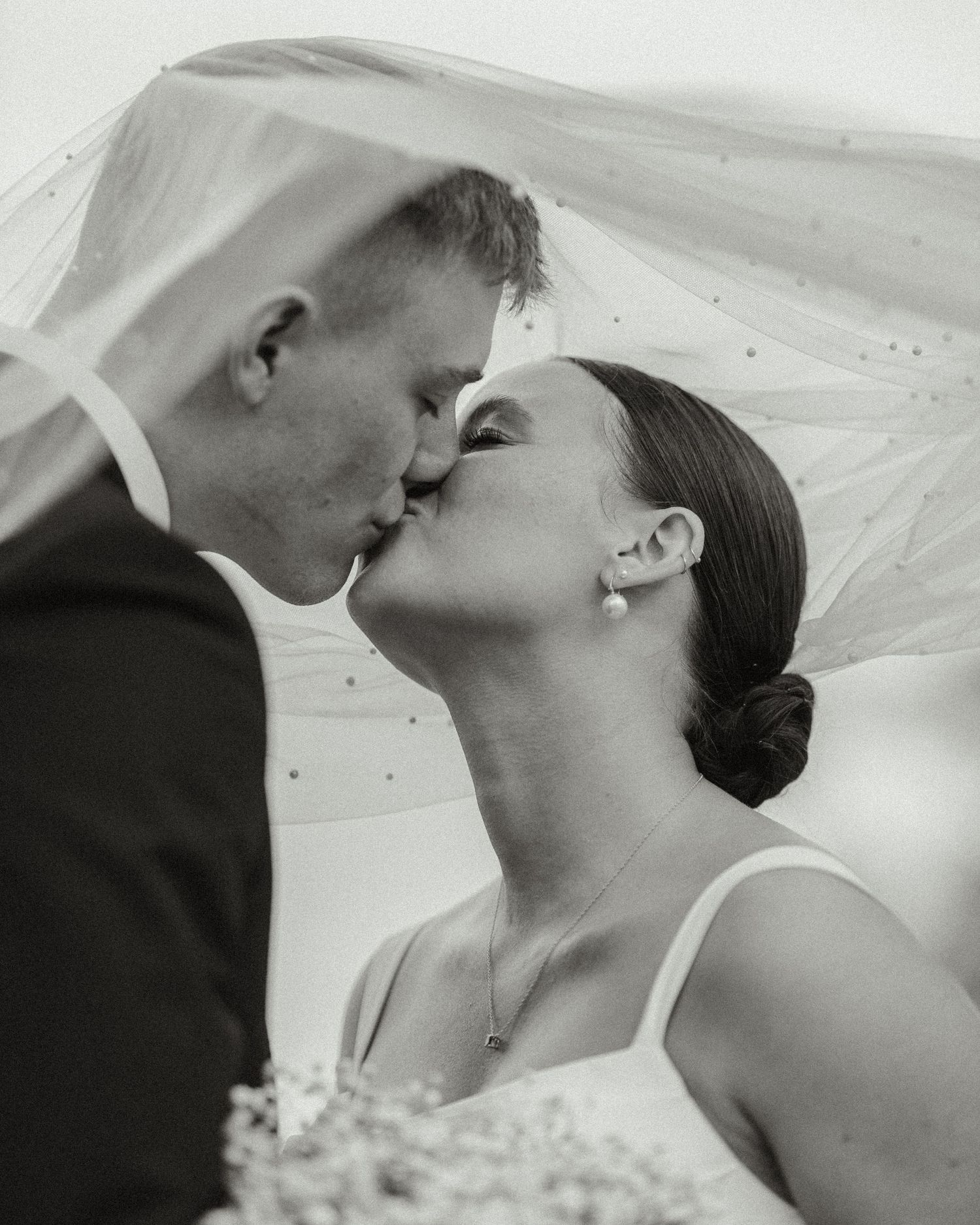A romantic black and white wedding photo showing a tender kiss under a delicate veil.