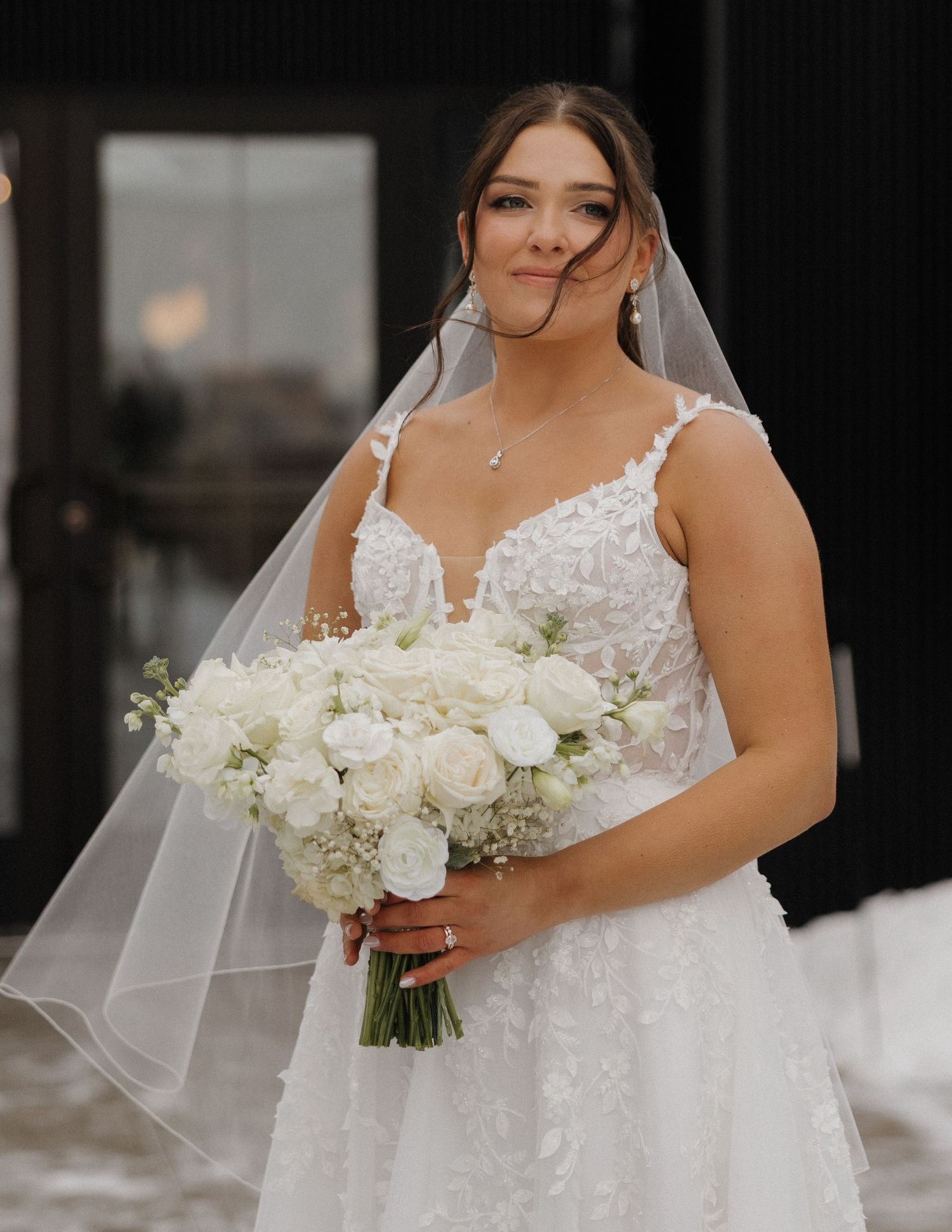 A bride in a white lace wedding dress holds a bouquet of white roses and flowers.