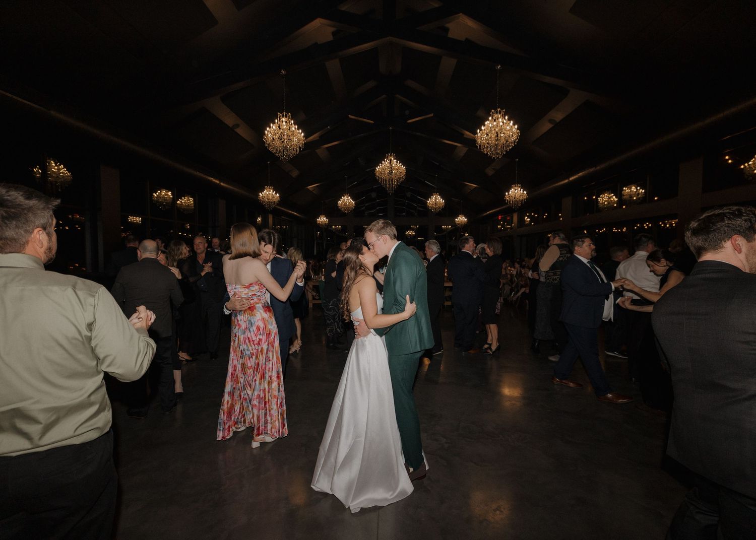 People dancing together in a dimly lit reception venue during a celebration event.