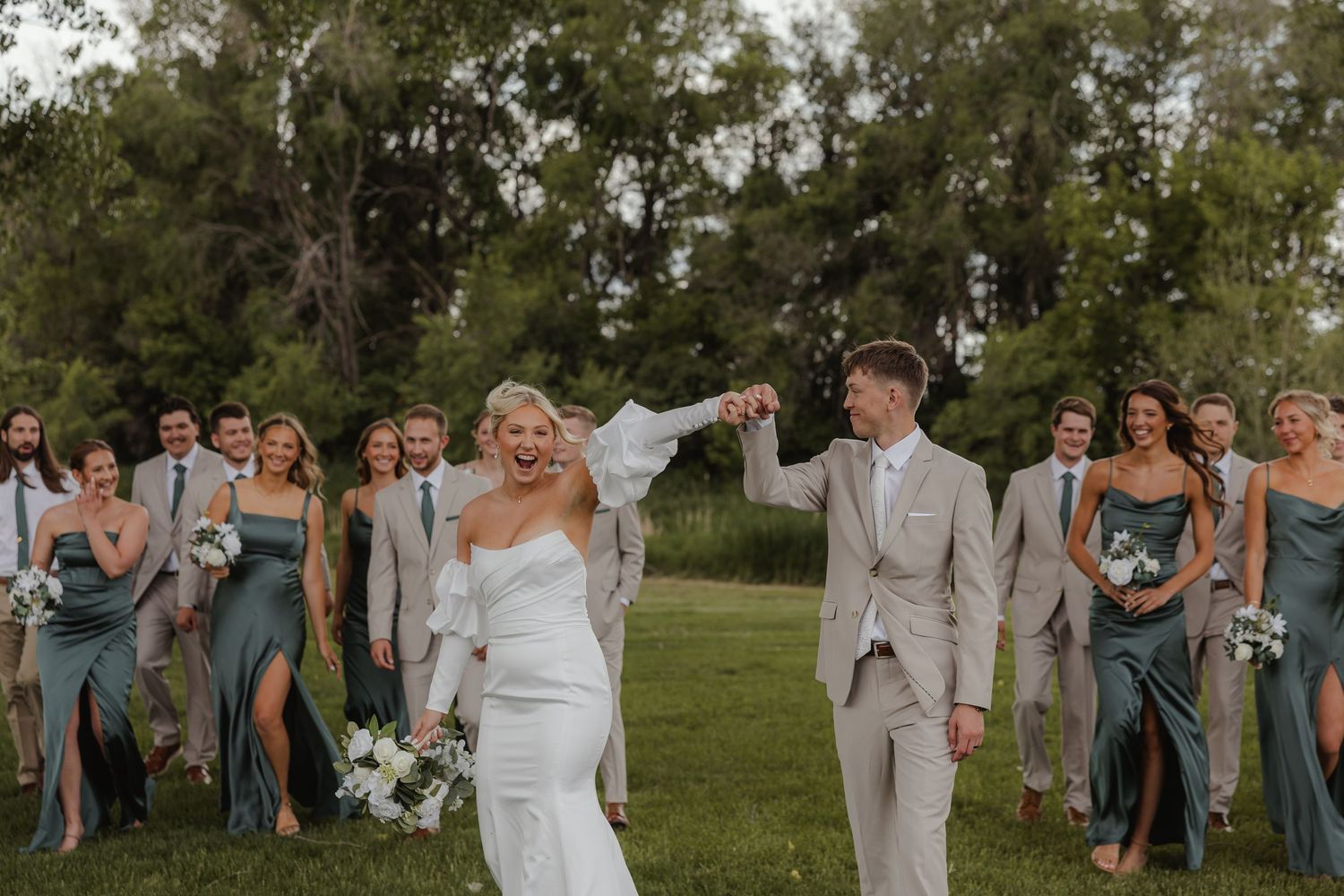Wedding party celebrates outdoors in a garden setting with bridesmaids in sage green dresses and groomsmen in gray suits.