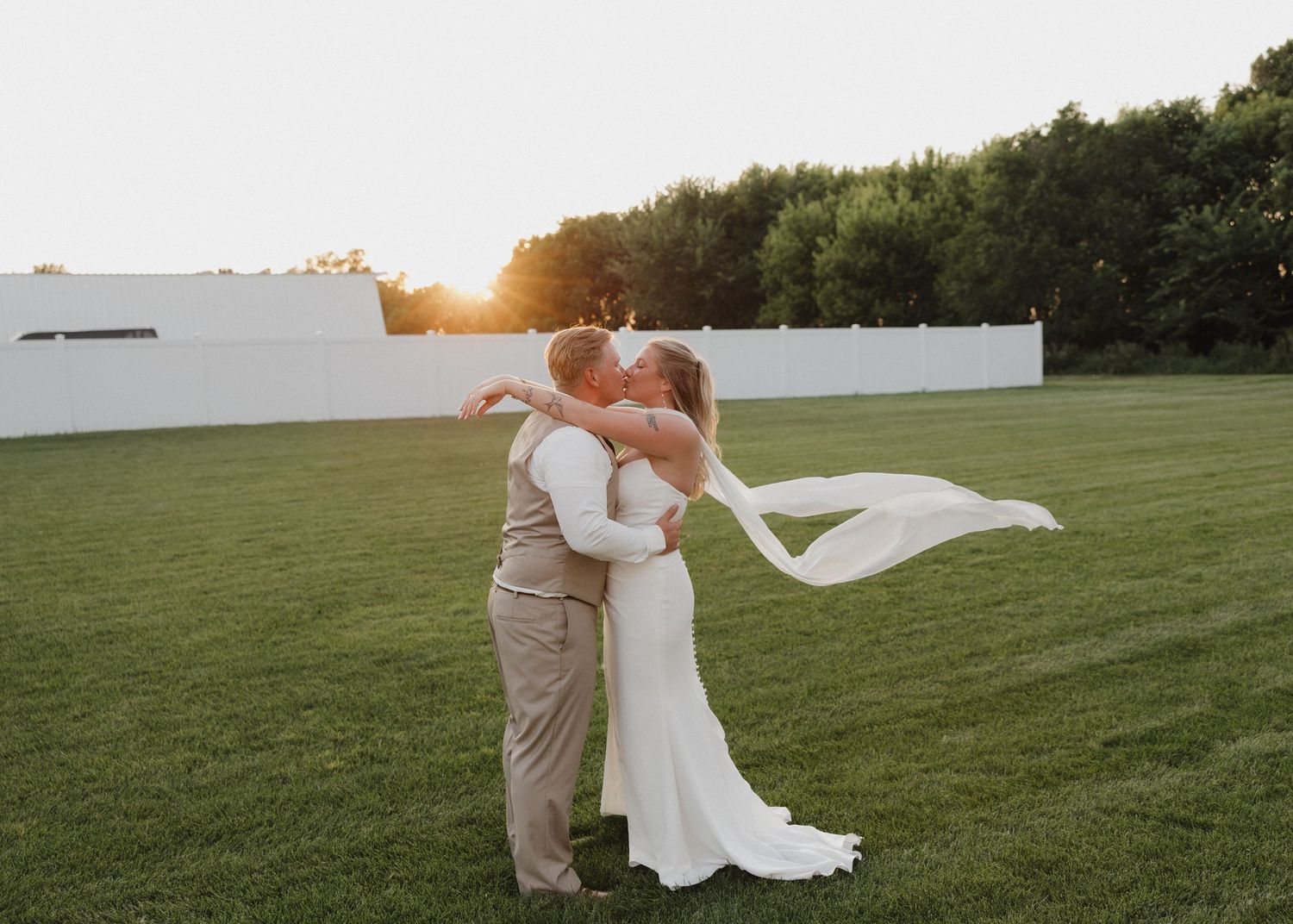 A flowing white dress billows in the wind against a green grassy field at sunset.