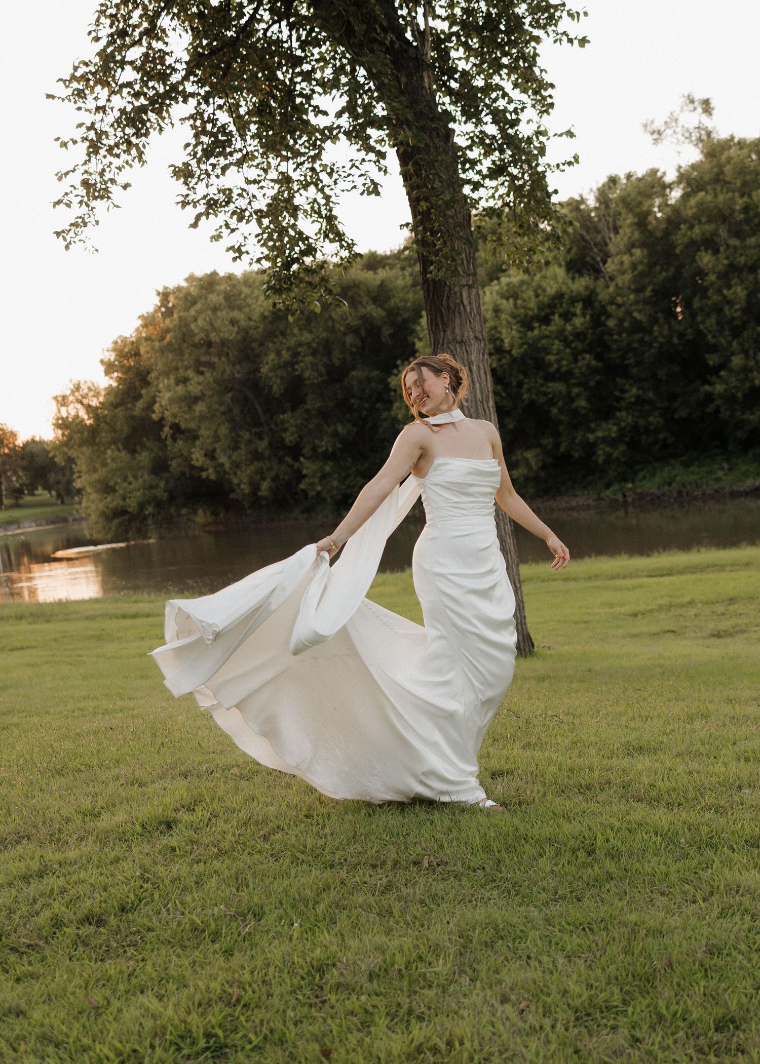 A flowing white wedding dress twirls gracefully across a sunlit grassy field during golden hour.