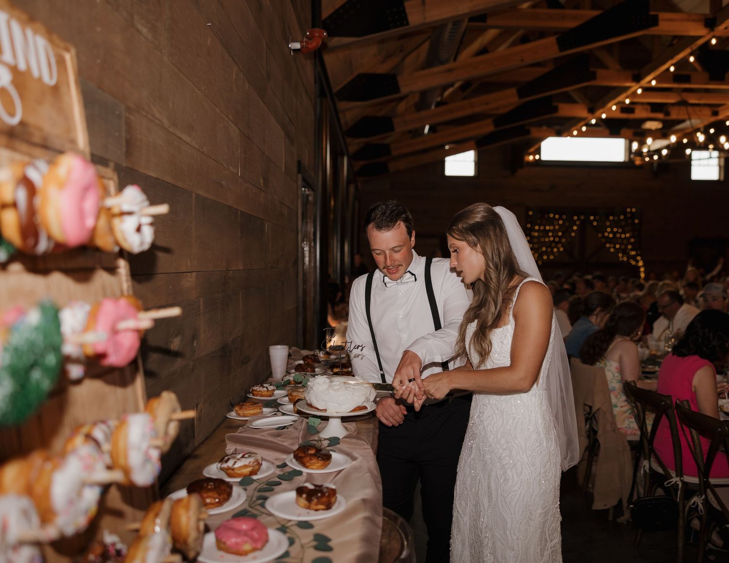 Couple looking at desserts displayed on a rustic table at a wedding reception with string lights in the background.