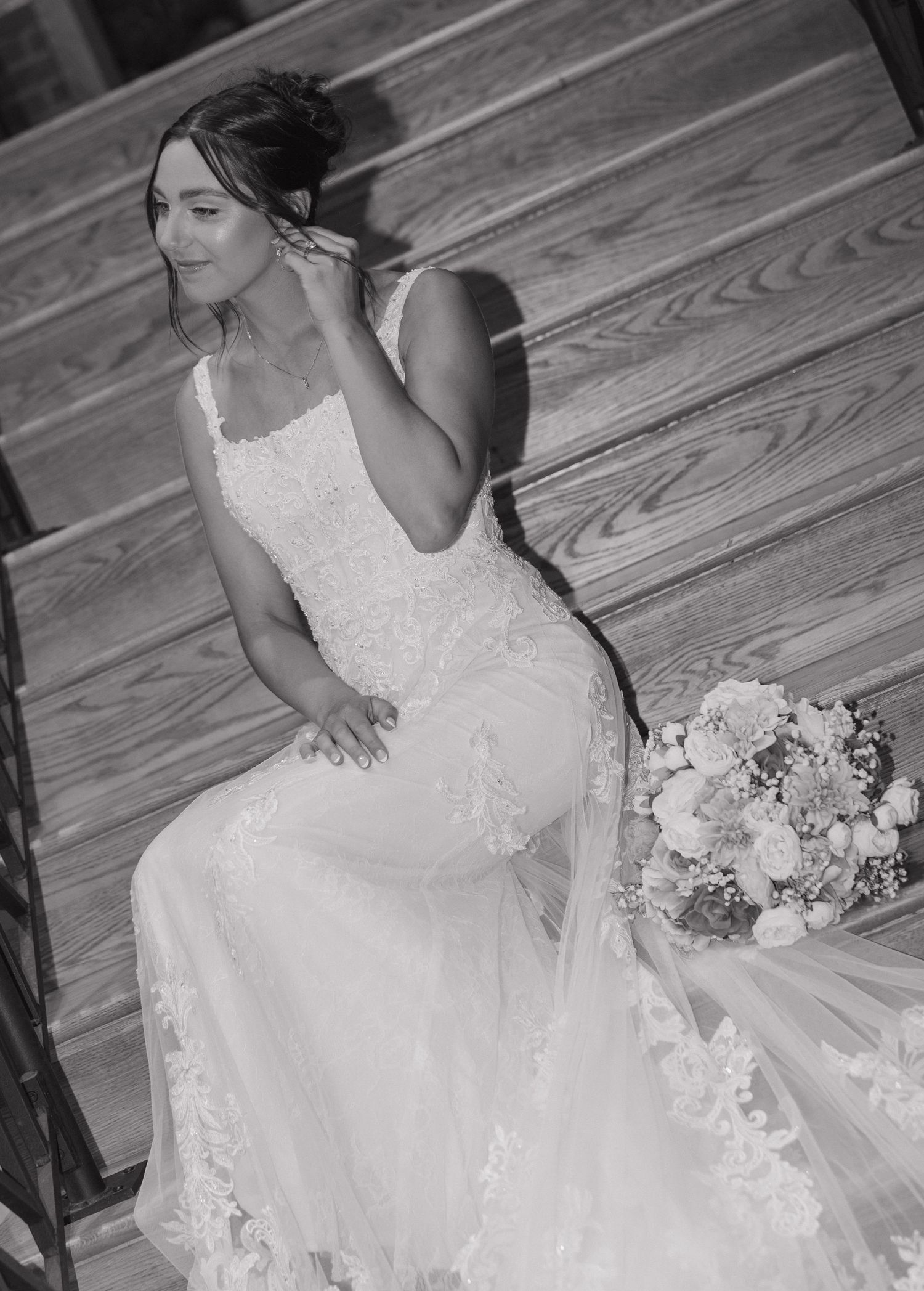 A bride in a white lace wedding dress poses on a wooden floor with a white and pink floral bouquet.