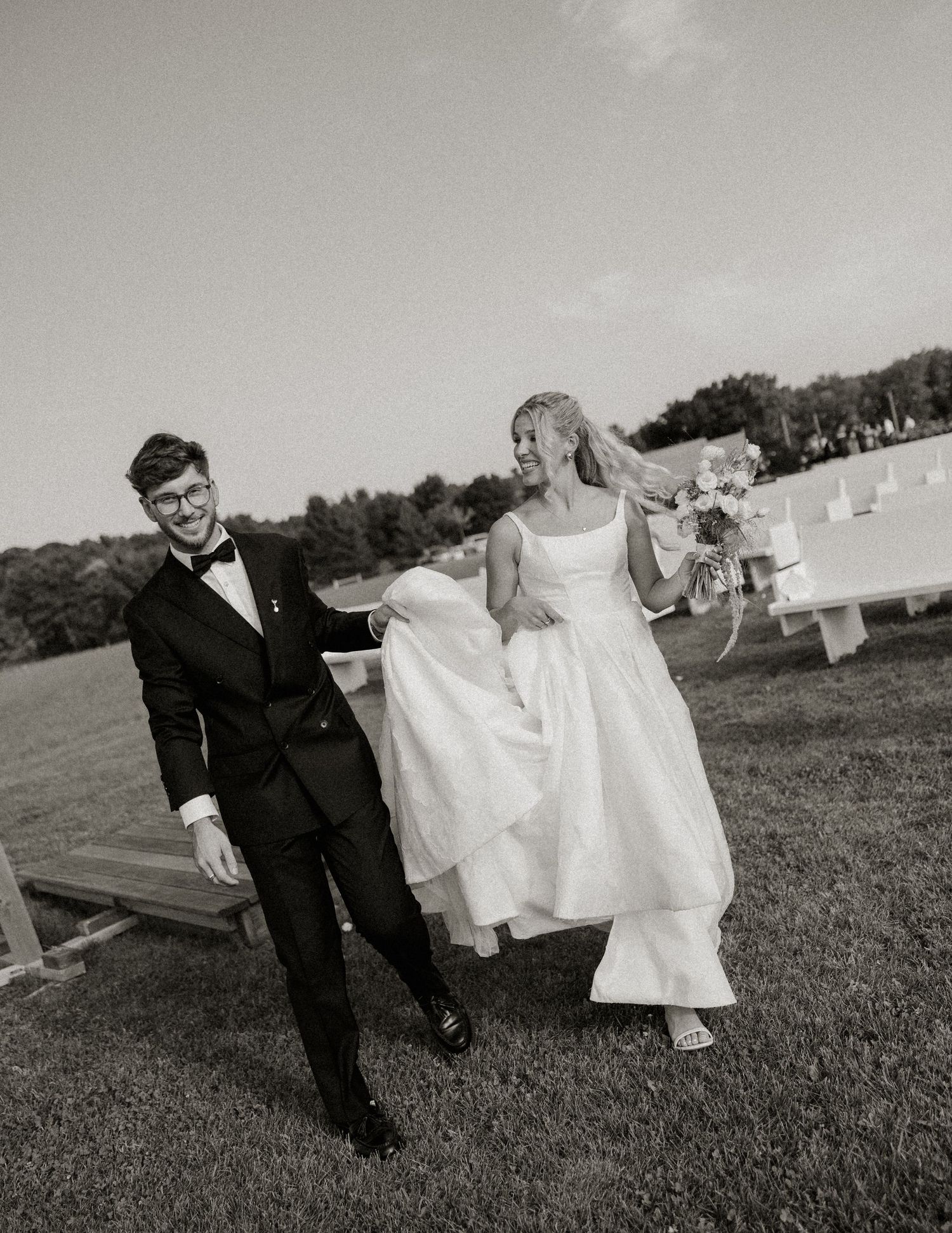 A couple in wedding attire playfully run and pose across a grassy field in a series of black and white photos.