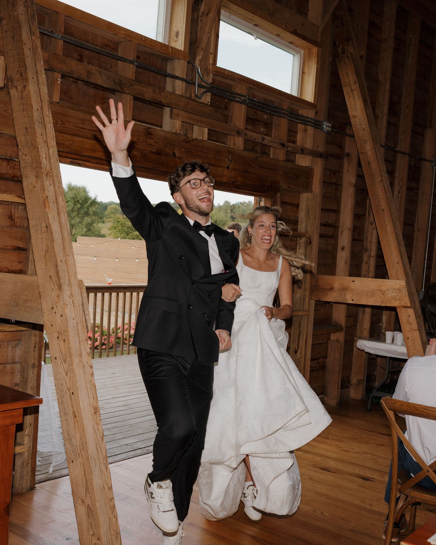 A couple dancing and twirling on a wooden floor in a rustic barn venue with exposed beams and natural lighting.