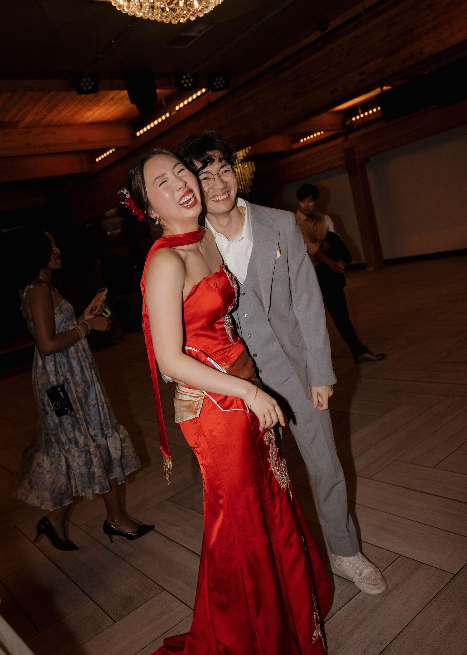 A couple in formal attire, with a red dress and grey suit, dancing together at an indoor event.