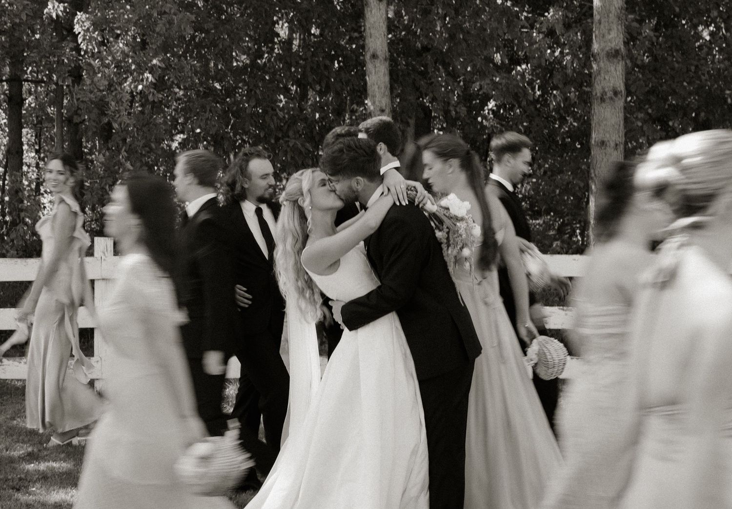 A group of people in formal white dresses dance in a circle outdoors during a celebration.