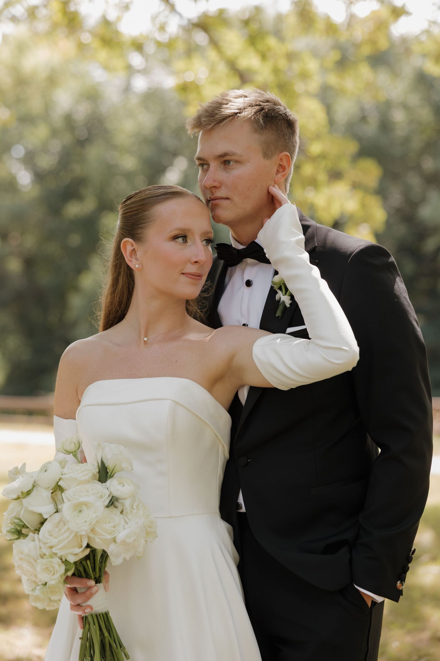 Romantic wedding couple embraces outdoors in autumn light while holding a white floral bouquet.