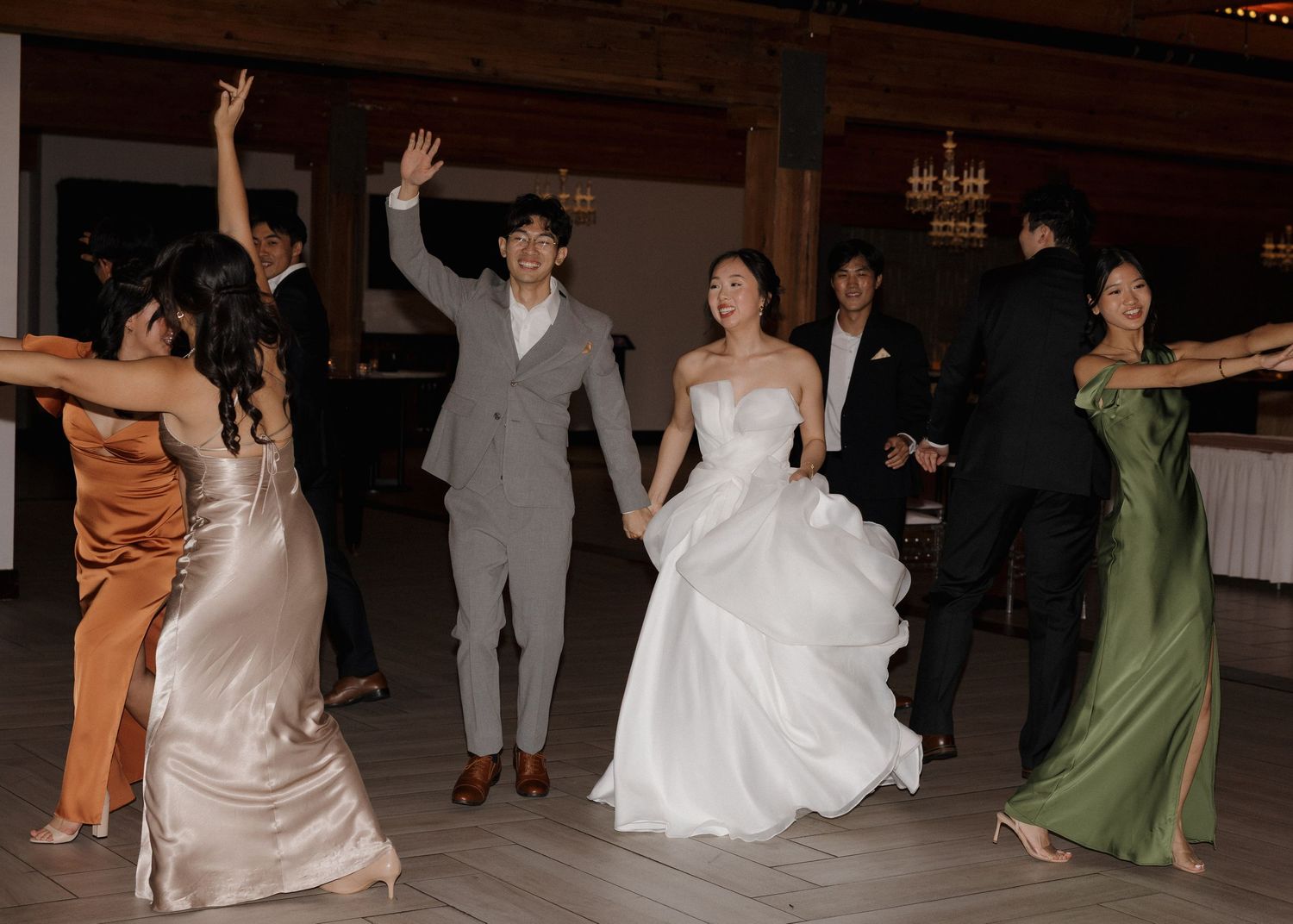 Wedding reception guests dancing and celebrating on a dark dance floor under chandeliers.