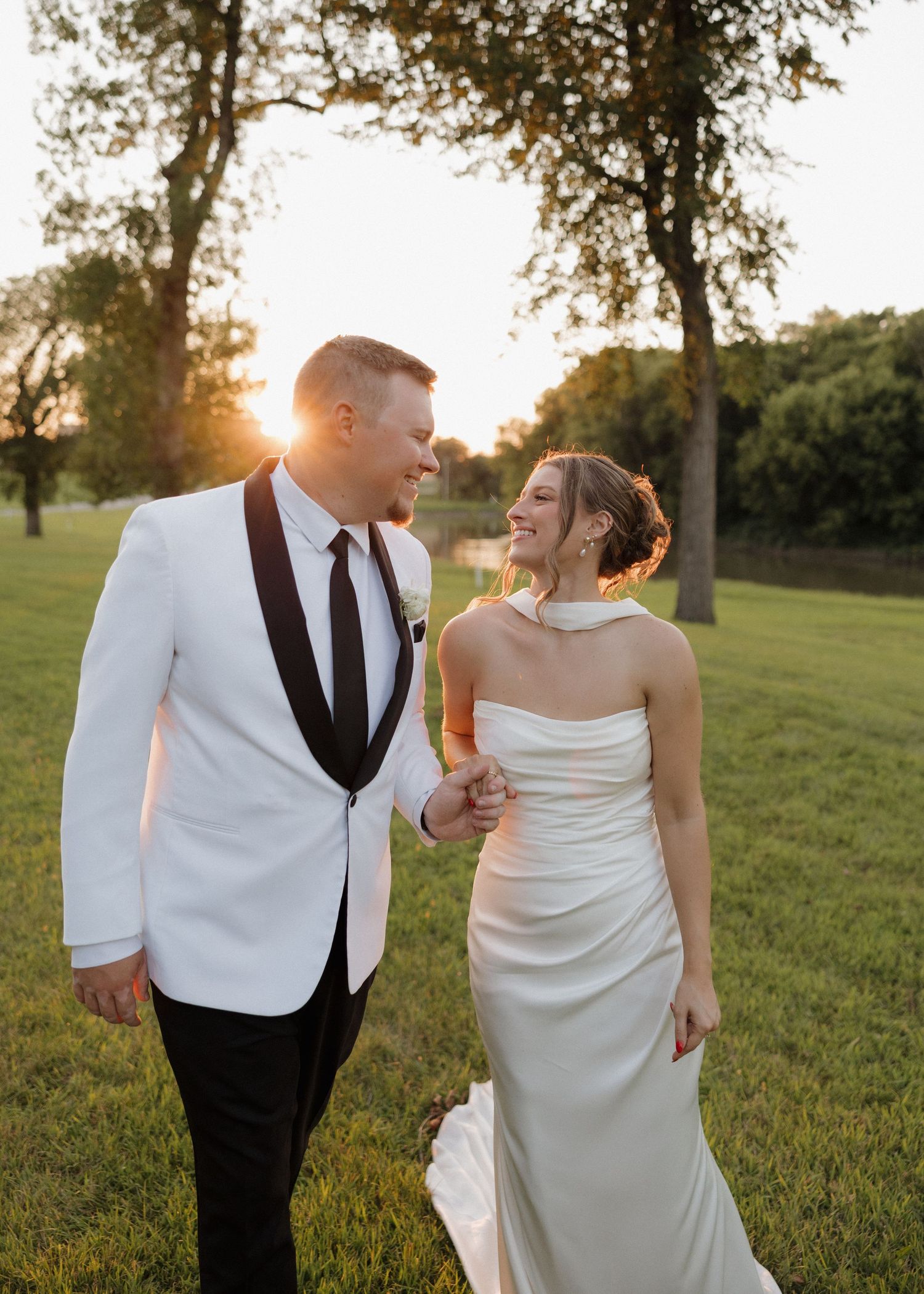 Elegant wedding couple shares intimate moment in grassy field during golden hour photography session.