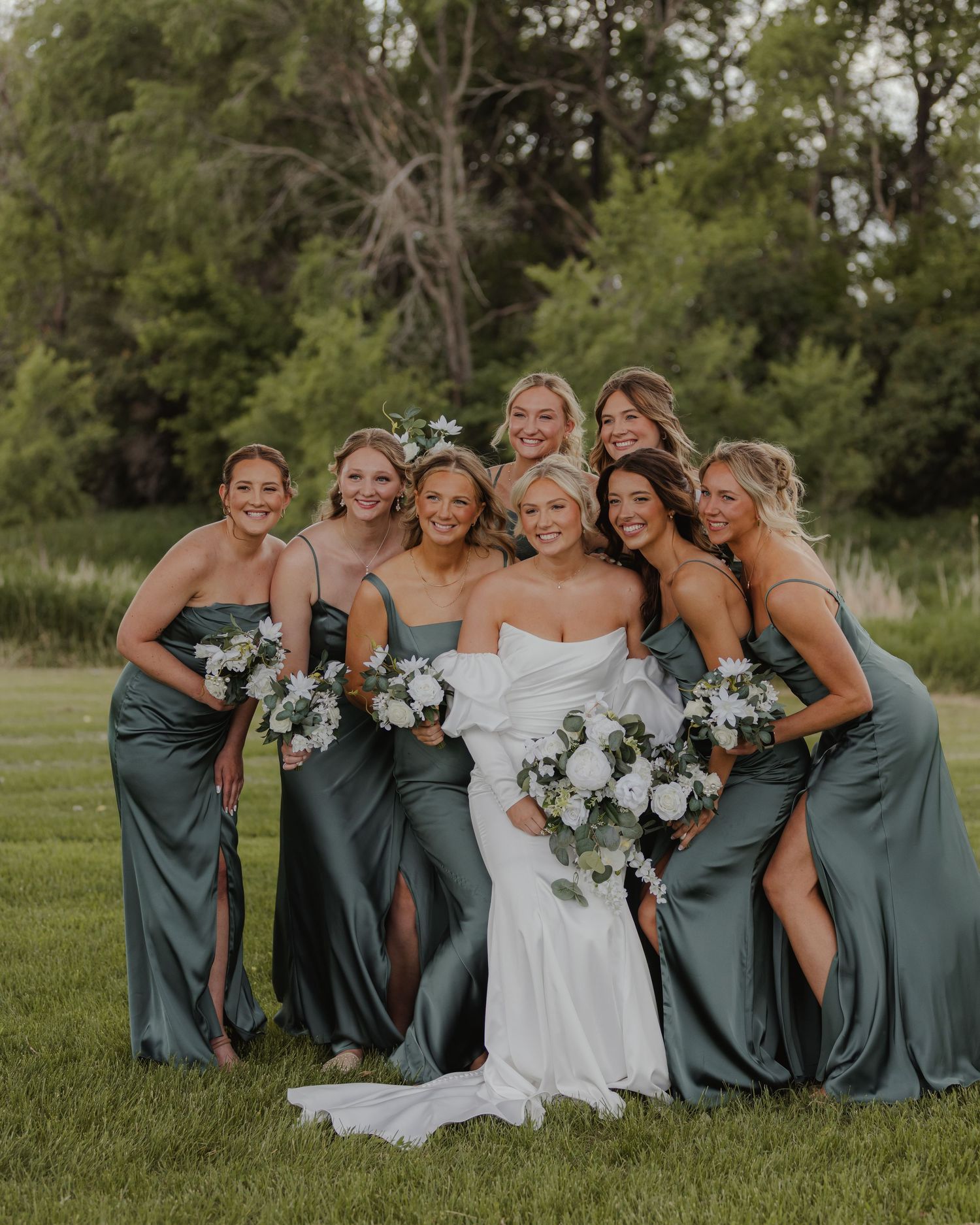 Bridesmaids in sage green dresses posing with bride on grassy lawn.
