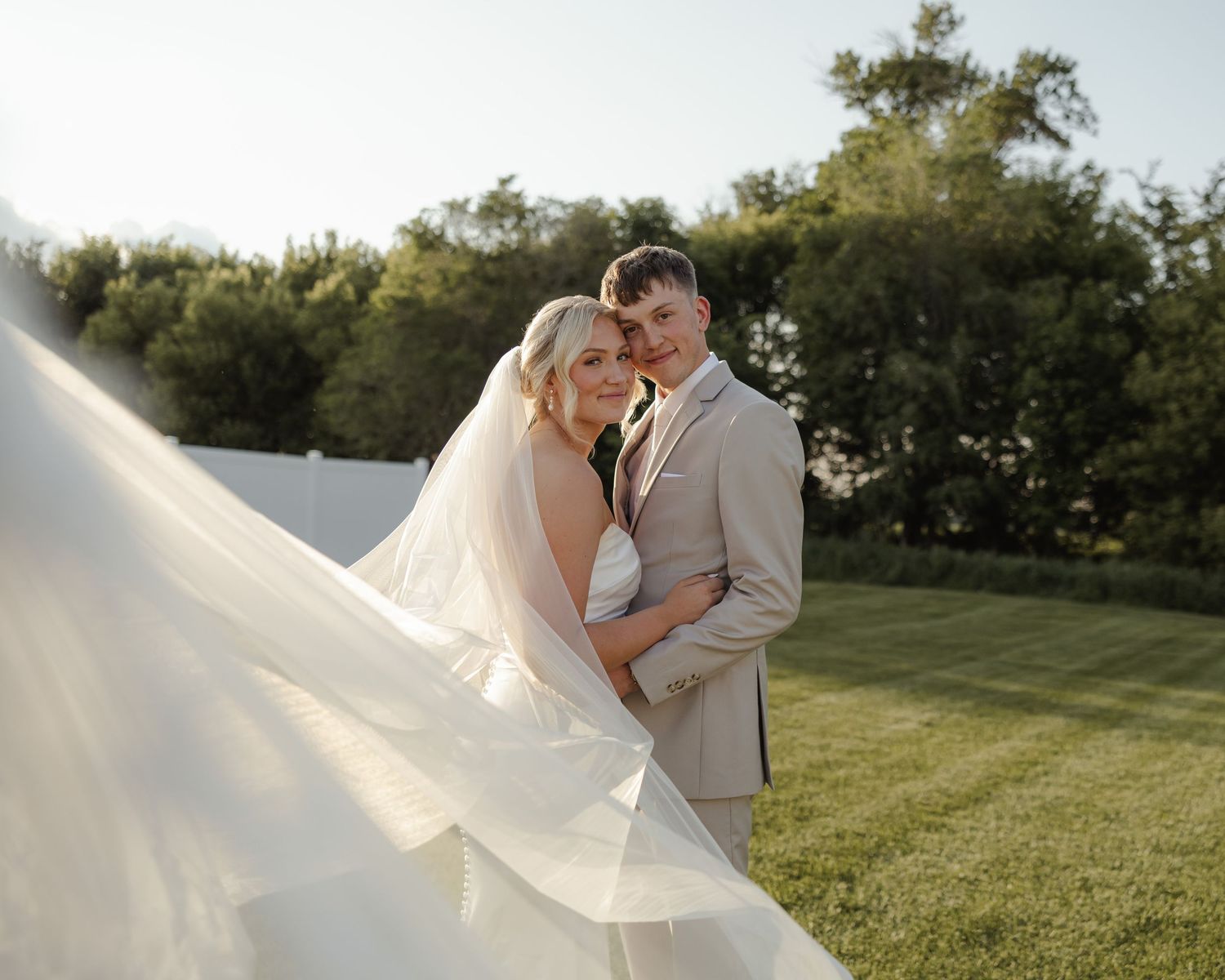Dreamy outdoor wedding portraits on a grassy hill with sunlit background.