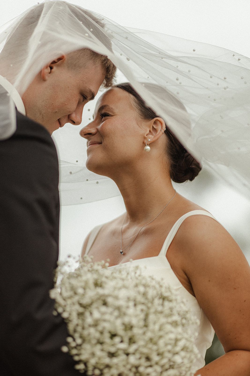 A romantic wedding portrait showing a tender moment between newlyweds with white baby's breath flowers in the foreground.