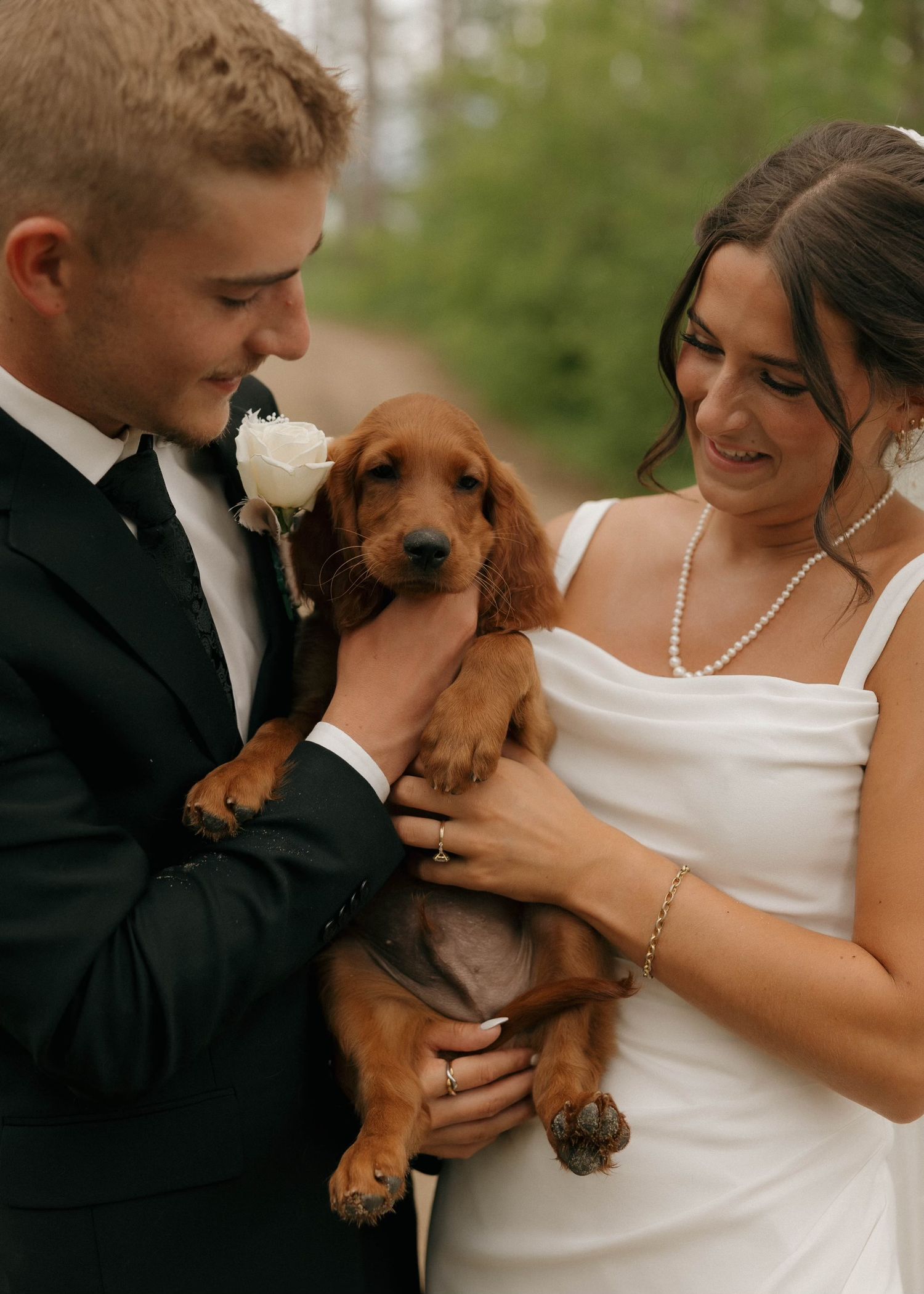 Newlyweds in formal attire hold their adorable golden retriever puppy during wedding photos.