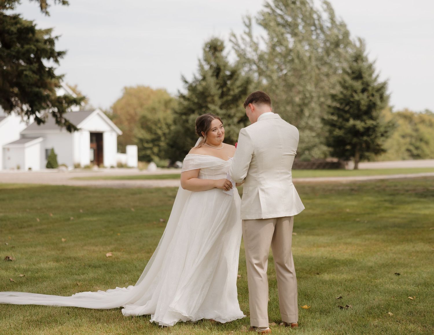 Couple in wedding attire dancing together on a grassy lawn during an outdoor celebration.