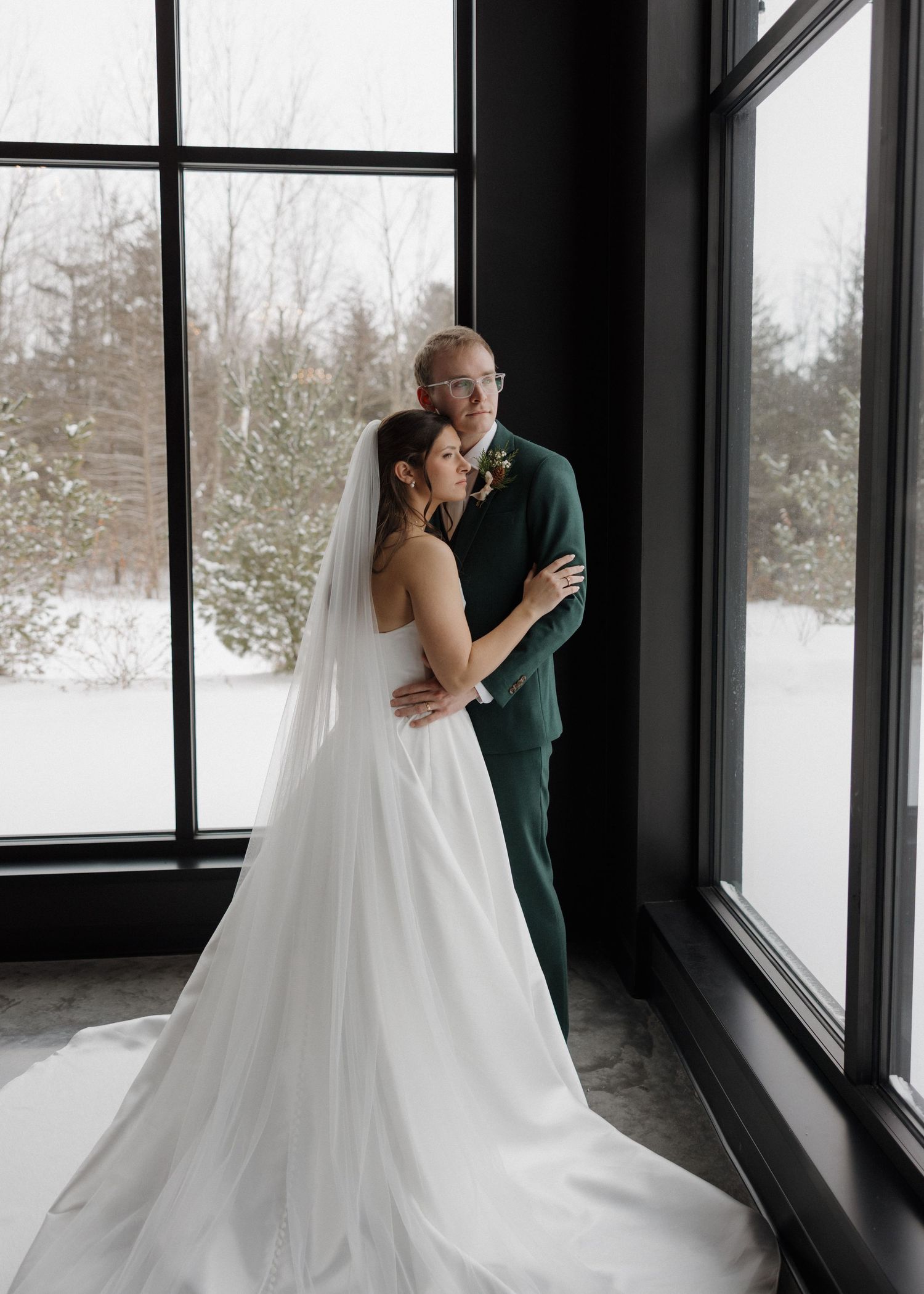 A romantic wedding couple shares intimate moments in a sunlit room with snowy winter views through large windows.